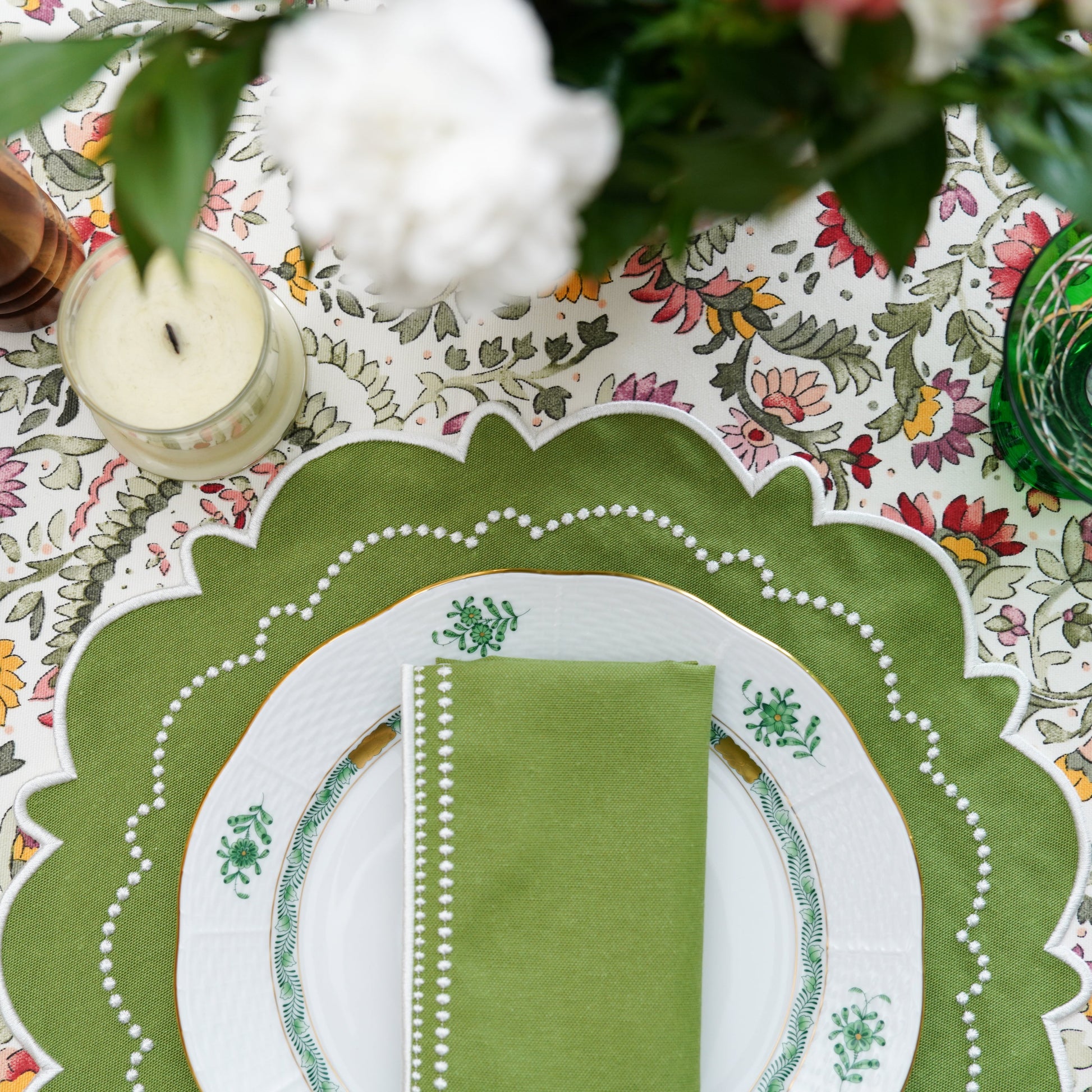 Detailed table setting with green napkin and place mat on a floral tablecloth.