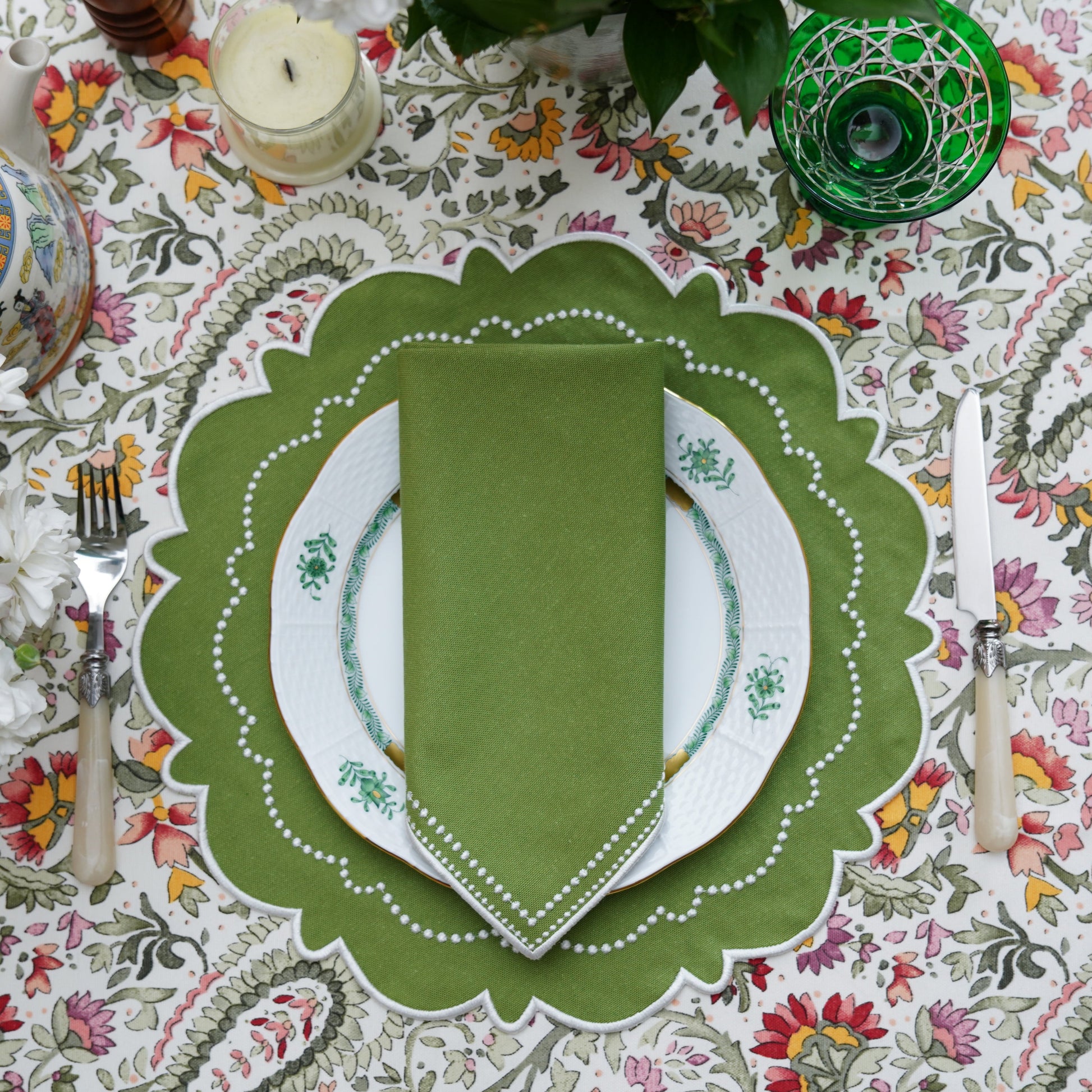 Elegant table setting with green placemat and floral tablecloth.