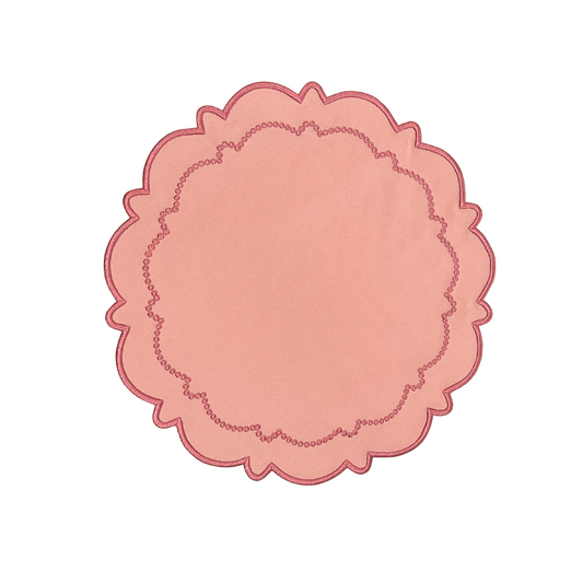 A round pink fabric placemat with a scalloped edge on a white background.