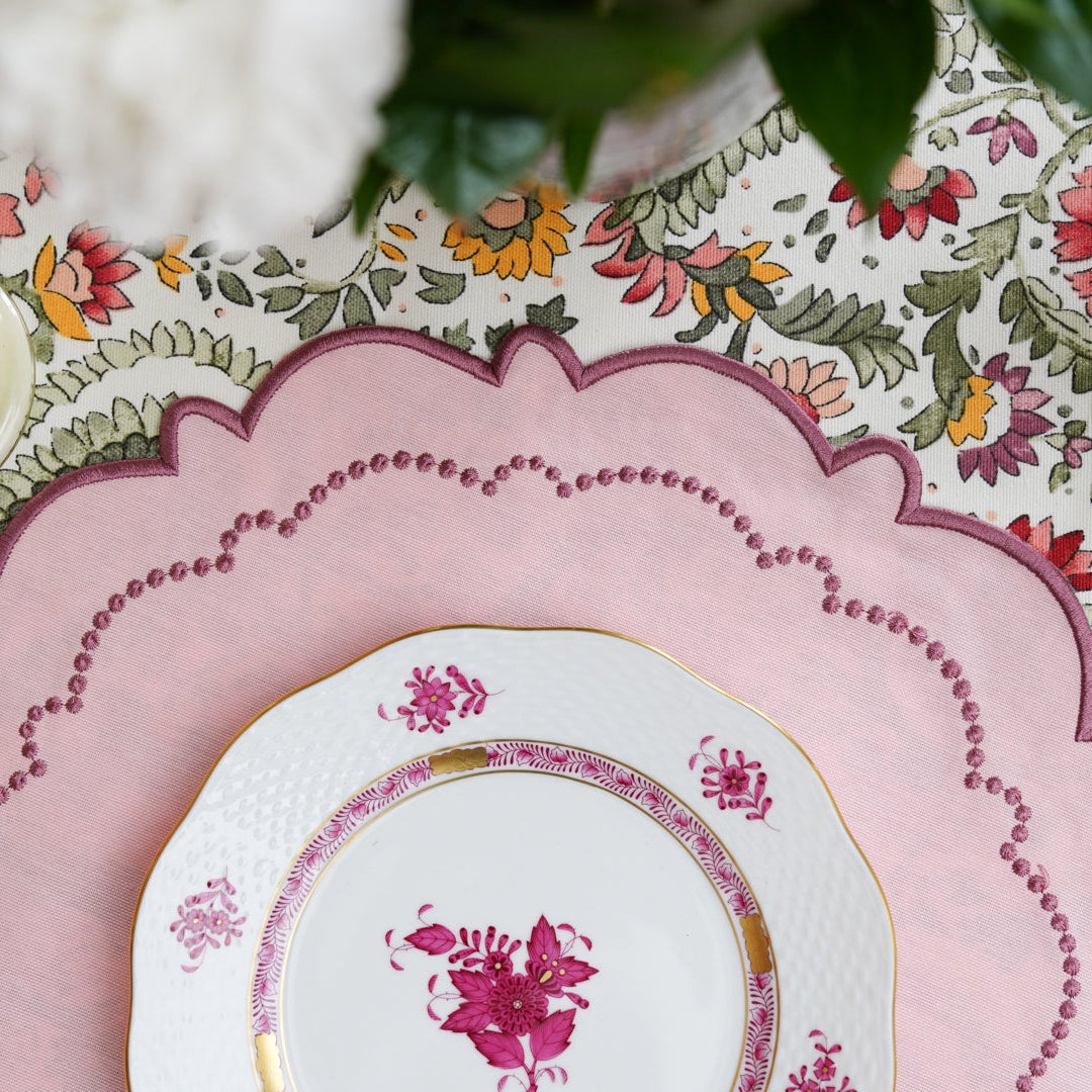 A pink floral fabric placemat with embroidered details, displayed on a table setting.