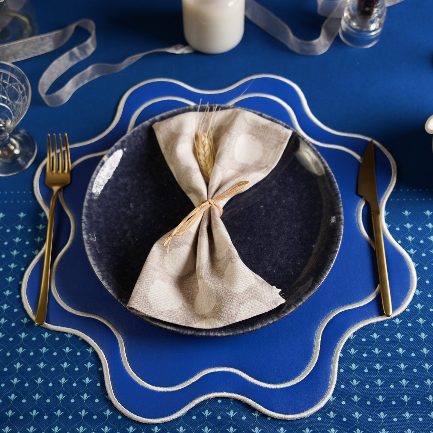 Napkin folded on a dark plate with cutlery on a blue patterned tablecloth