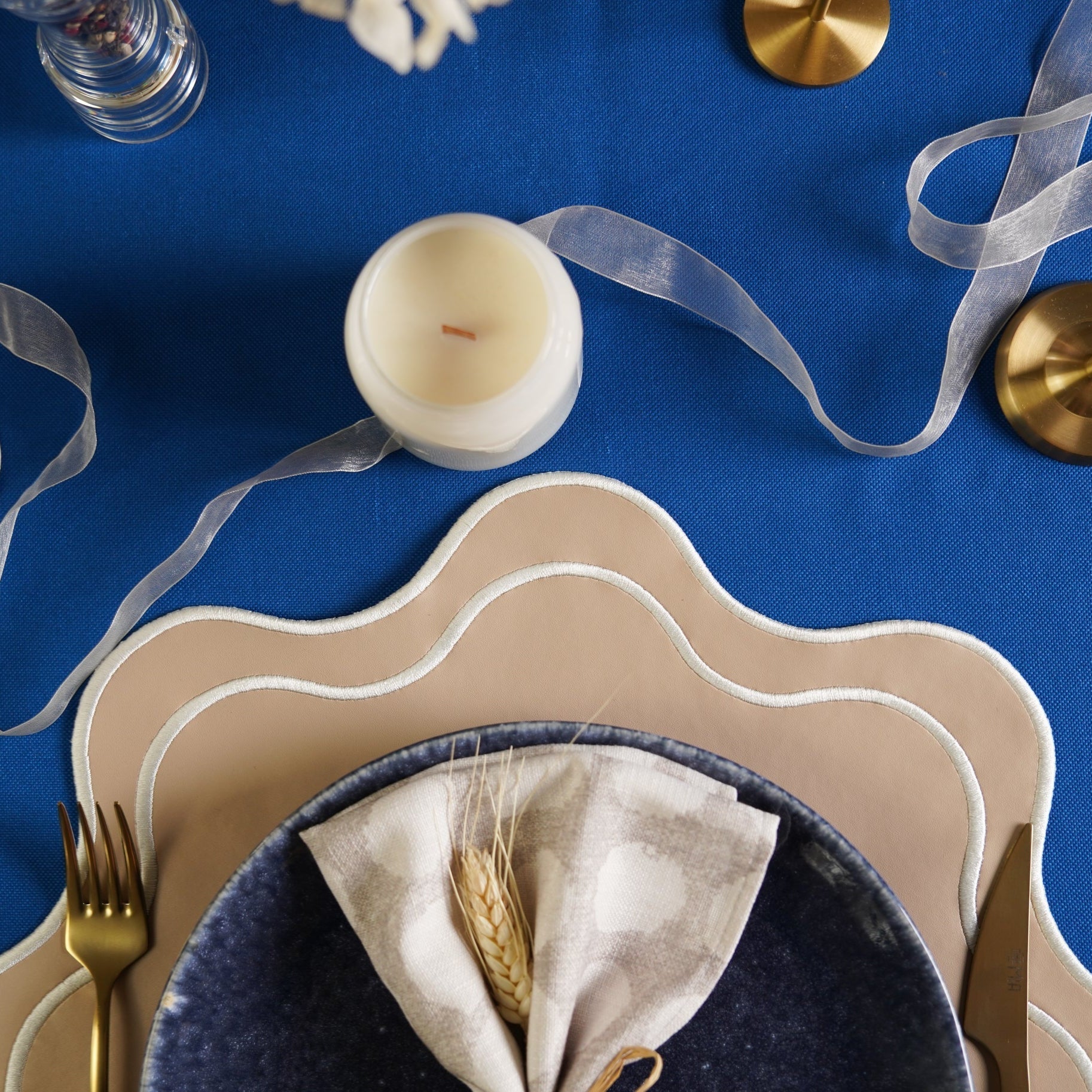 Table setting with a candle, plates, napkin, and gold fork on a blue tablecloth.