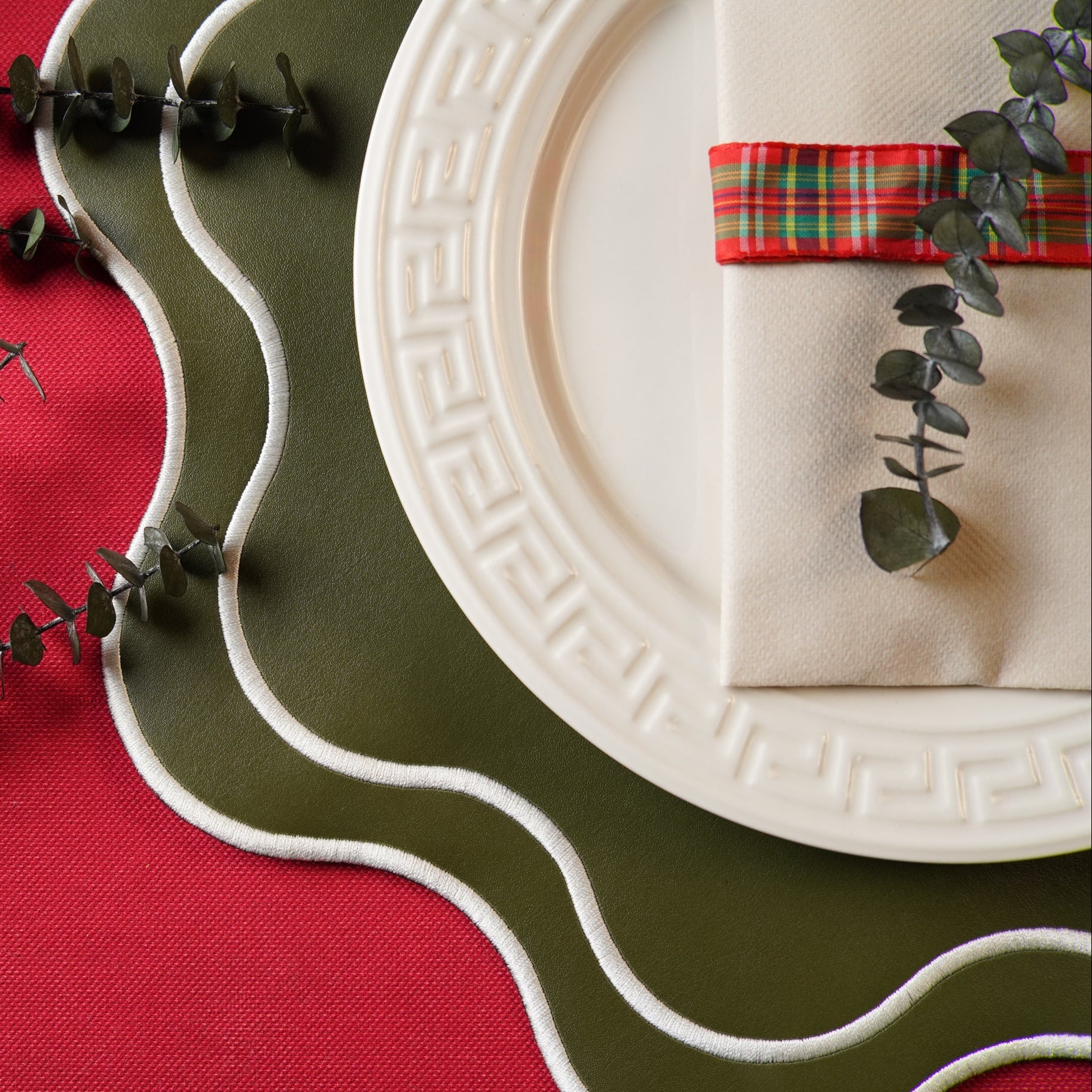 Decorative table setting with a white plate, green placemat, and red napkin on a red tablecloth.