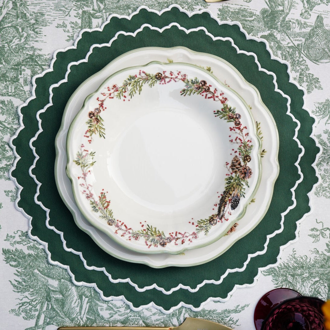 A set of embroidered placemats with a green and white floral pattern displayed on a table with dishes and cutlery.