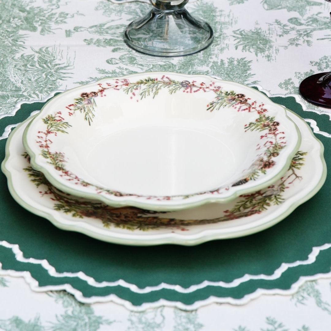 Set of white dishes with floral patterns on a tablecloth with green borders.