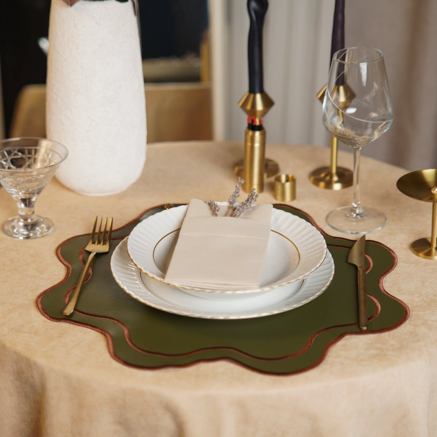 Elegant table setting with white plates, gold cutlery, and green placemat on a beige tablecloth.