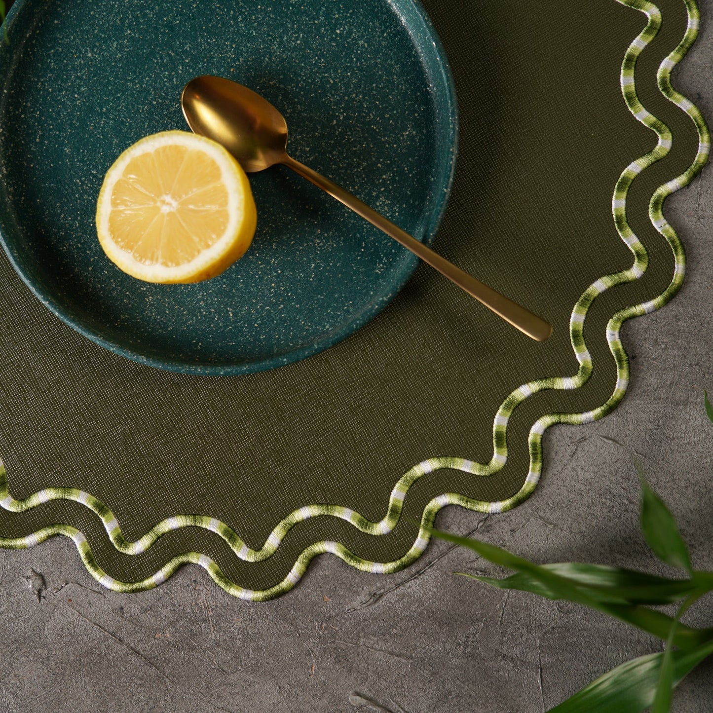 Green plate with a lemon and gold spoon on a textured surface