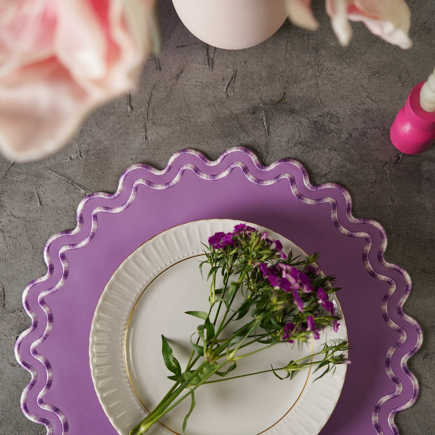 Purple decorative plate with a white plate featuring purple flowers on a gray surface.