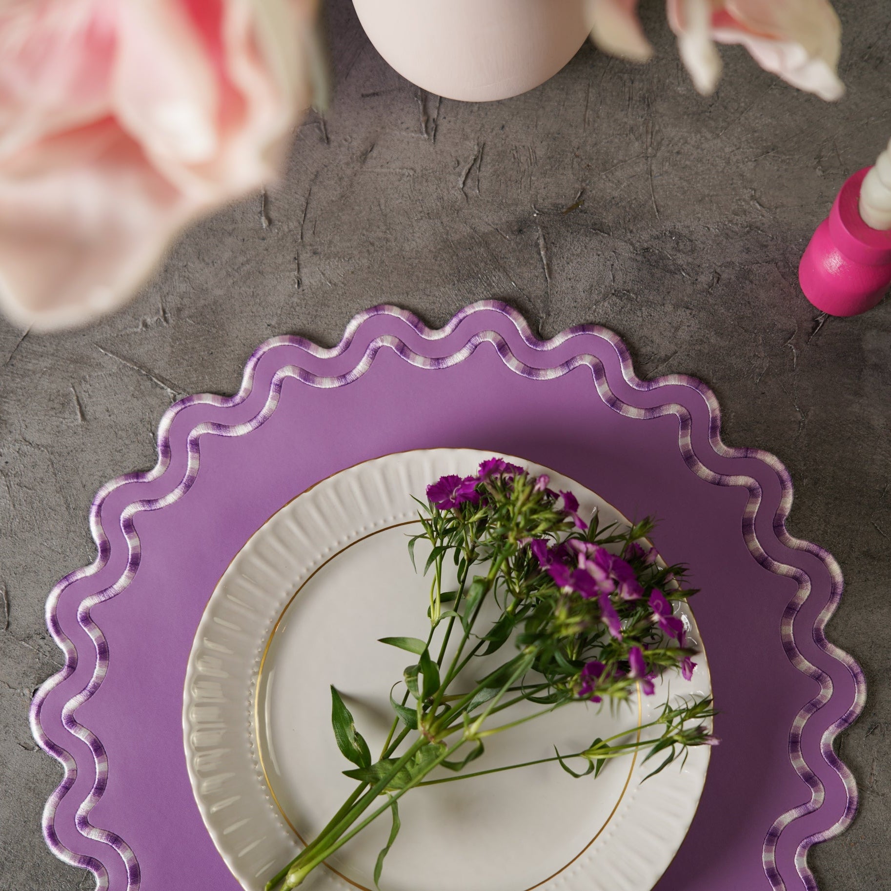 Purple decorative plate with a white plate featuring purple flowers on a gray surface.