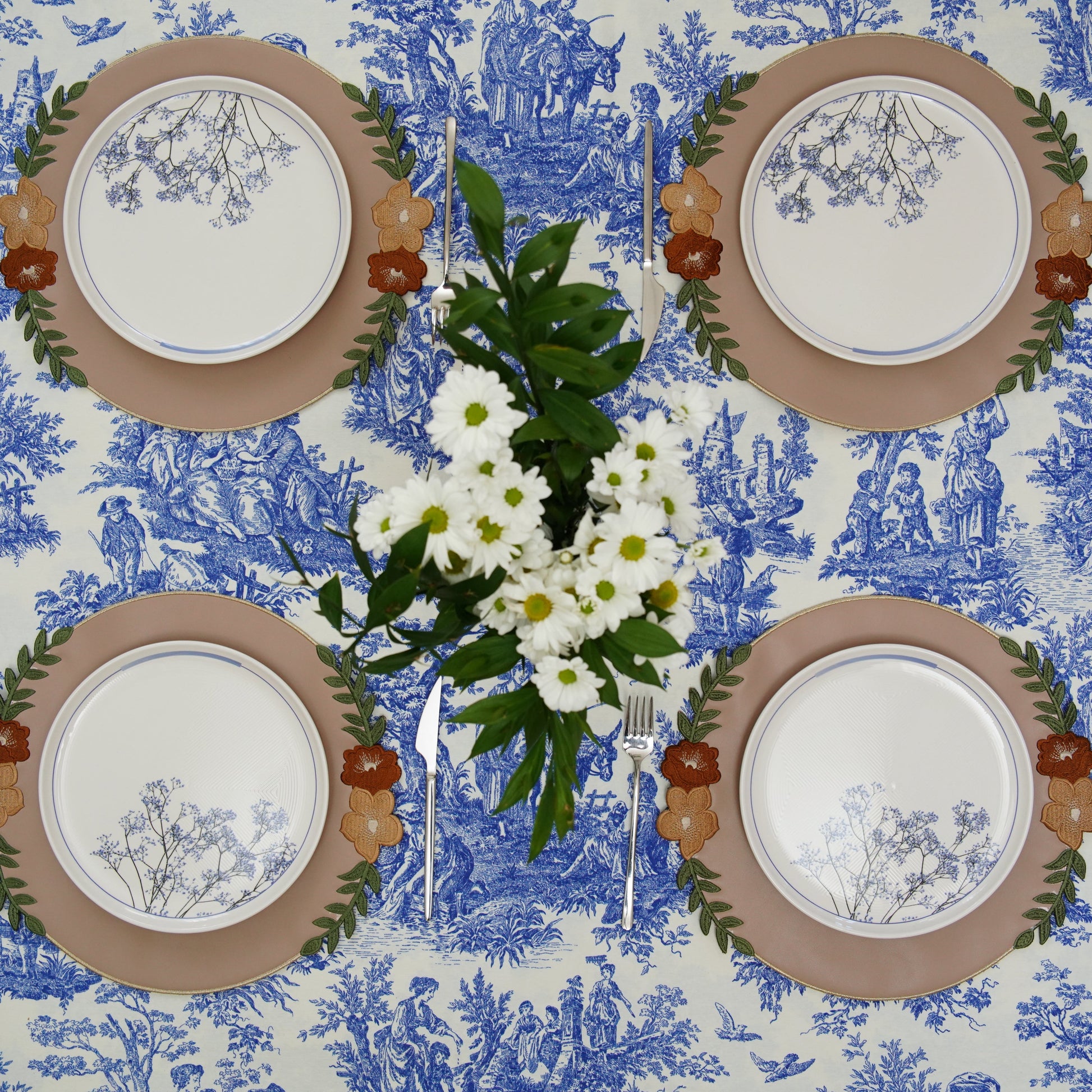 Set of four plates with decorative borders on a blue and white patterned tablecloth.