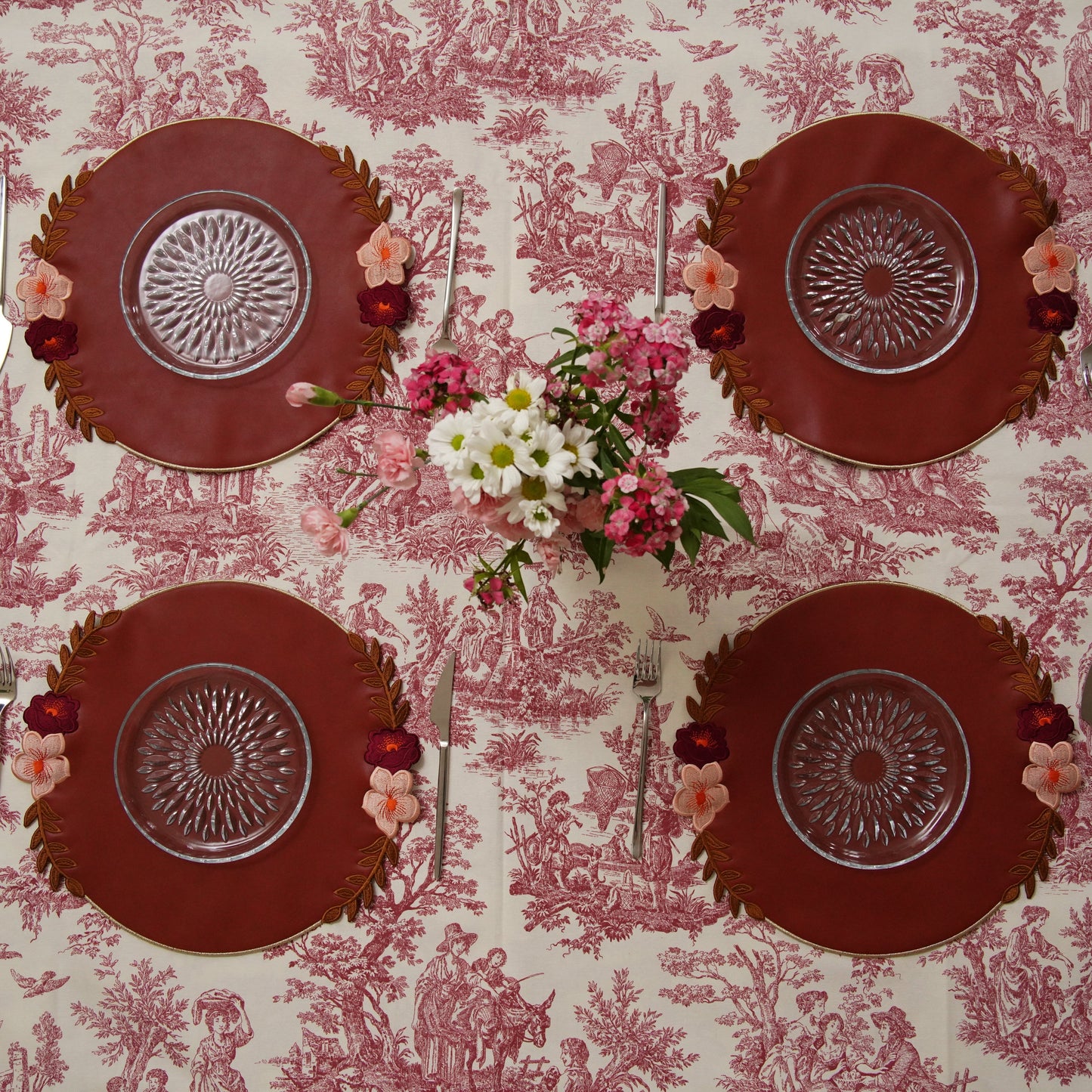 Set of four red plates with decorative patterns on a pink toile tablecloth.