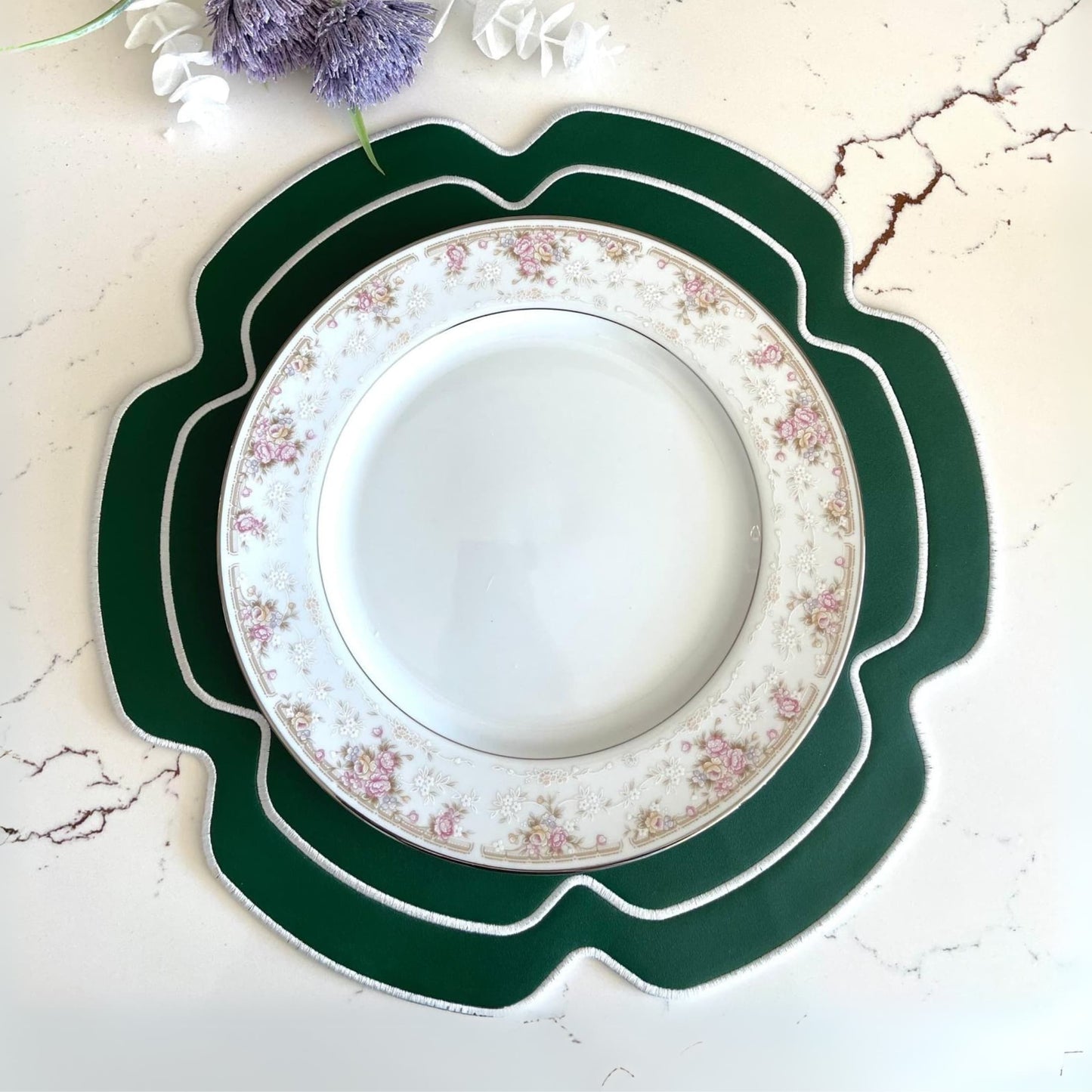 A round green faux leather placemat with a decorative pattern, displayed under a white plate with floral design.