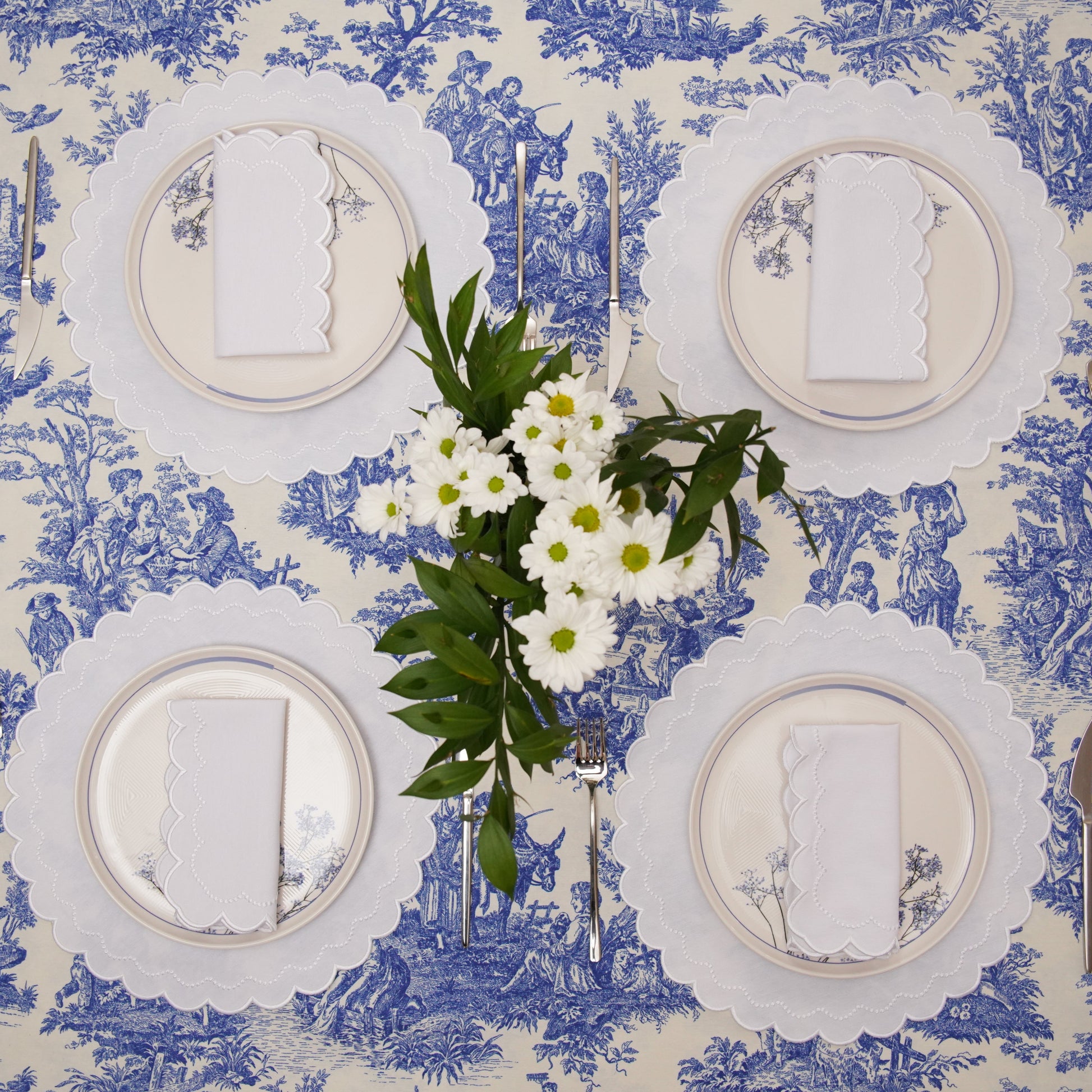 Table setting with white plates, silverware, and a floral centerpiece on a blue and white patterned tablecloth.