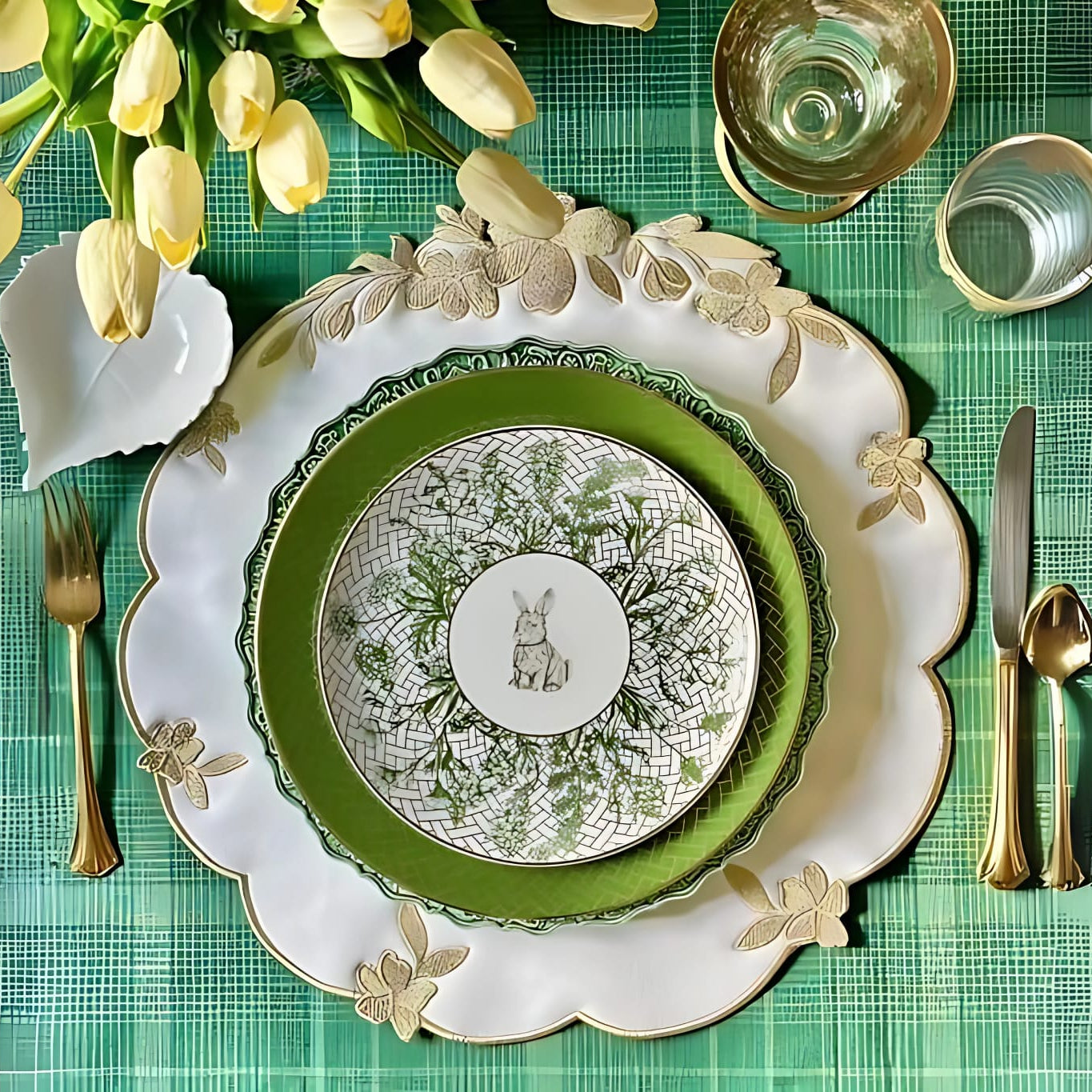 A set table with white and gold faux leather placemats, surrounded by green placemats, with a white plate and silverware in the center. A vase with yellow tulips is also visible on the table.