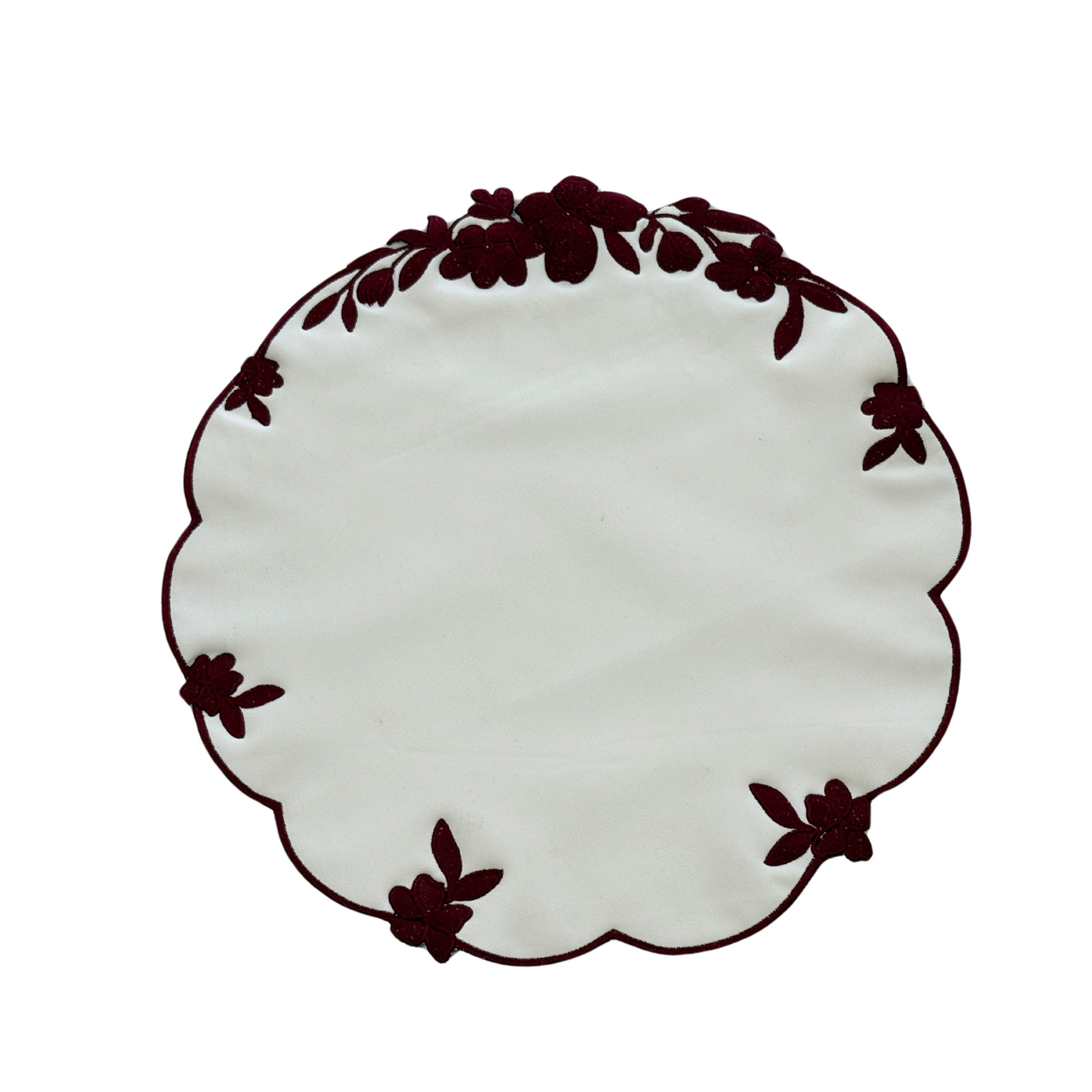 A round white faux leather placemat with burgundy floral embroidery around the edge.