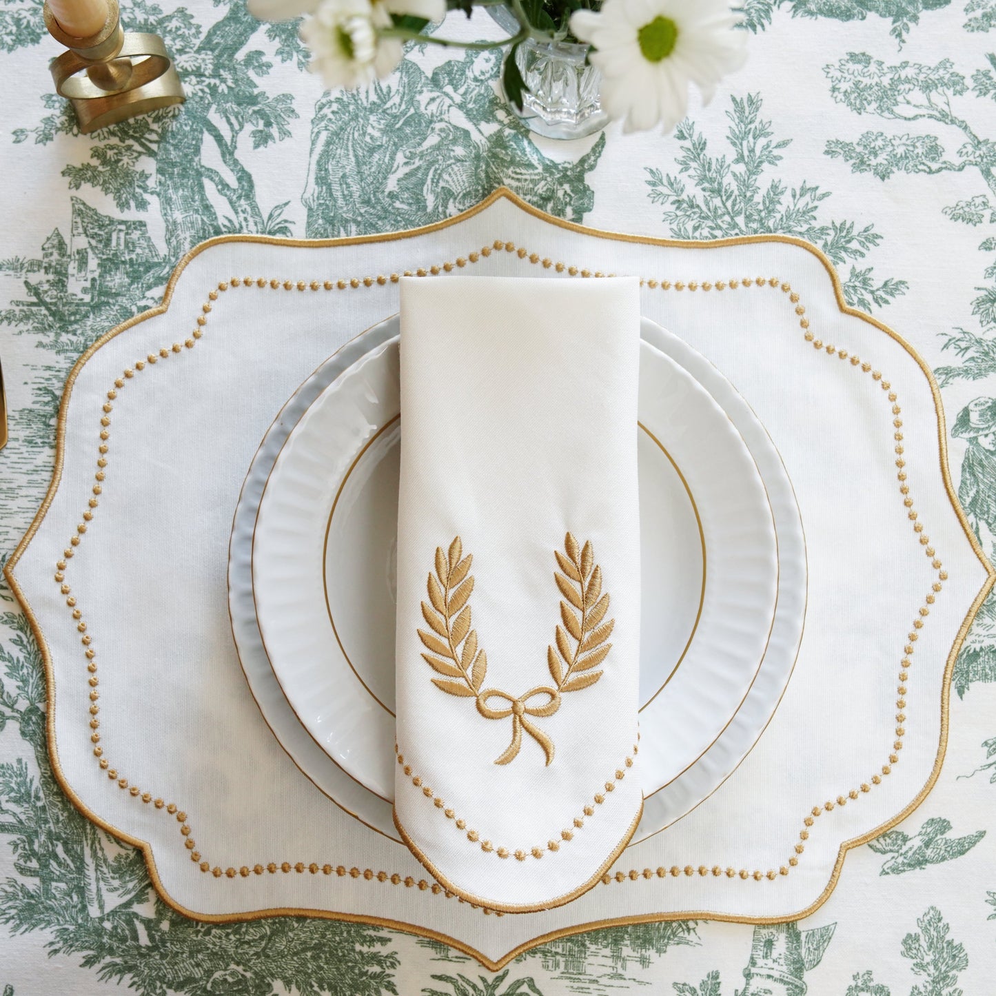 Elegant table setting with gold cutlery and decorative plates on a patterned tablecloth.