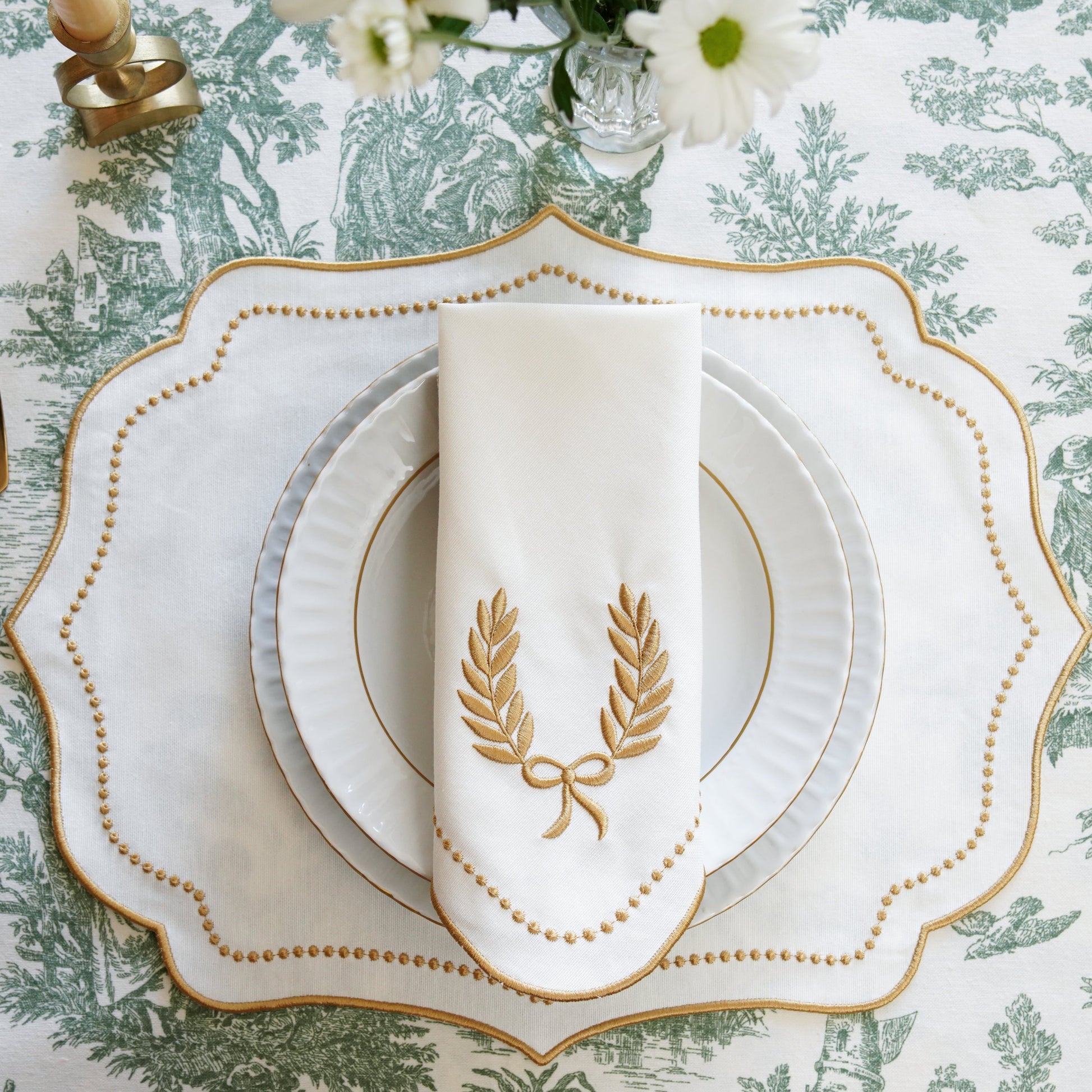 Elegant table setting with gold cutlery and decorative plates on a patterned tablecloth.
