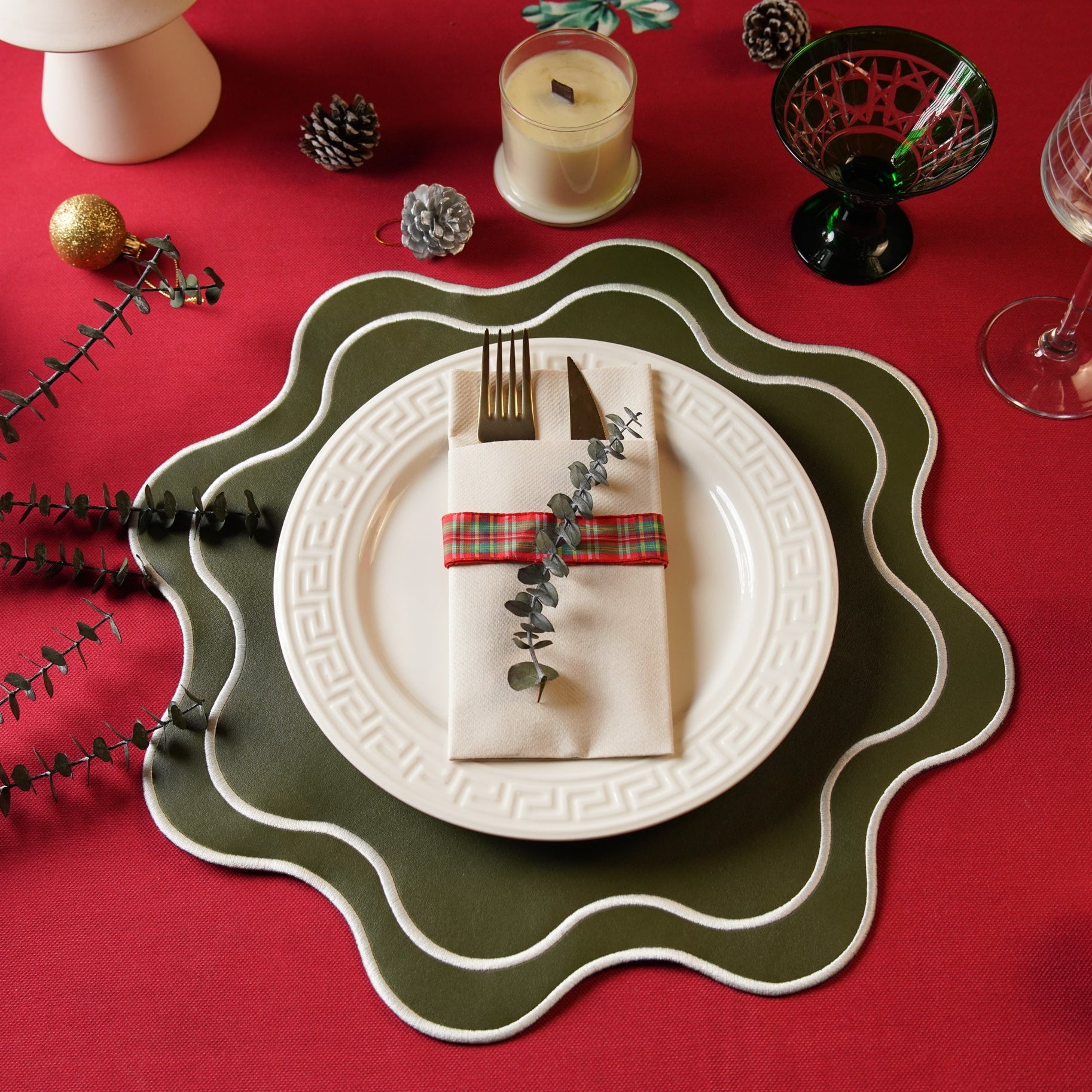 Christmas table setting with a white plate, green charger, and red napkin on a red tablecloth.