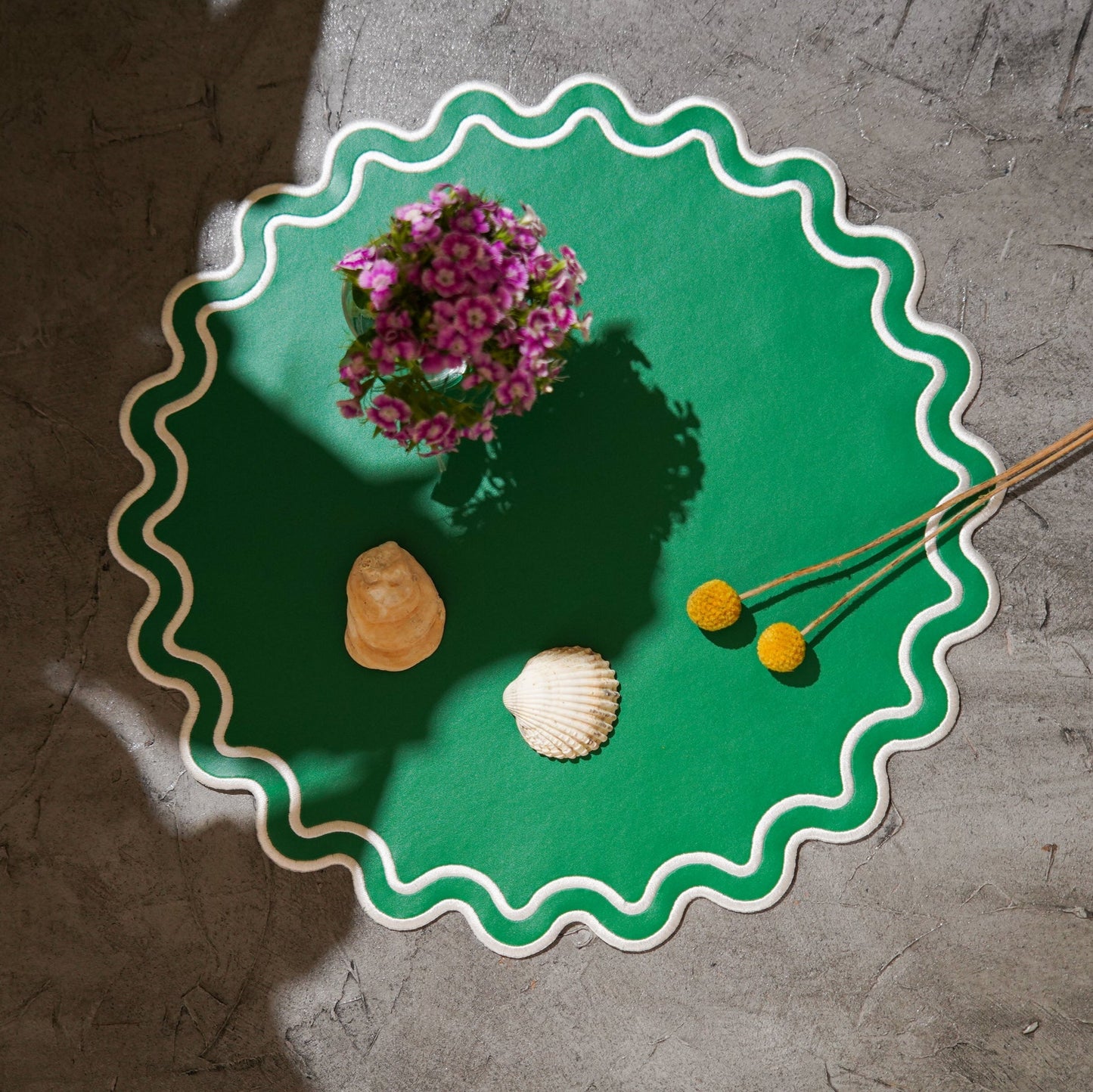 Green decorative plate with floral arrangement, shells, and dried plants on a textured surface