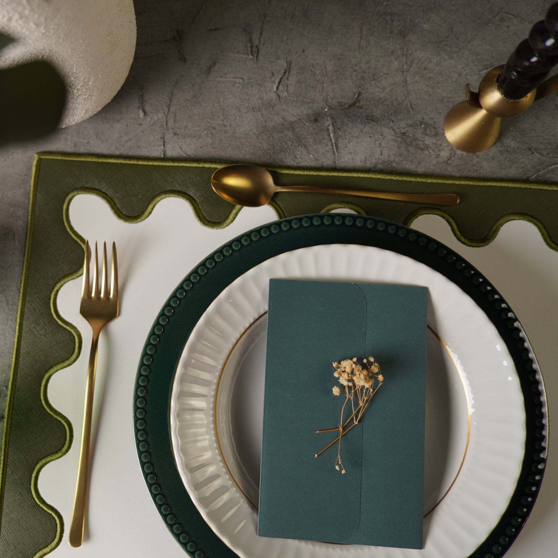 Dining table setting with green napkin, gold spoon, and fork on a textured surface.