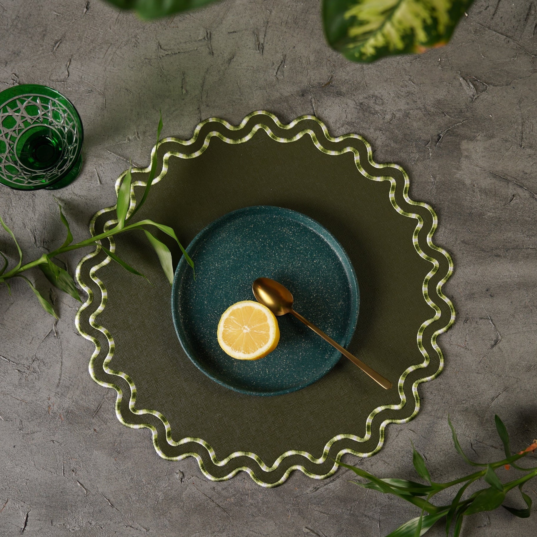 Decorative green plate with a blue center, lemon, and spoon on a textured gray surface.