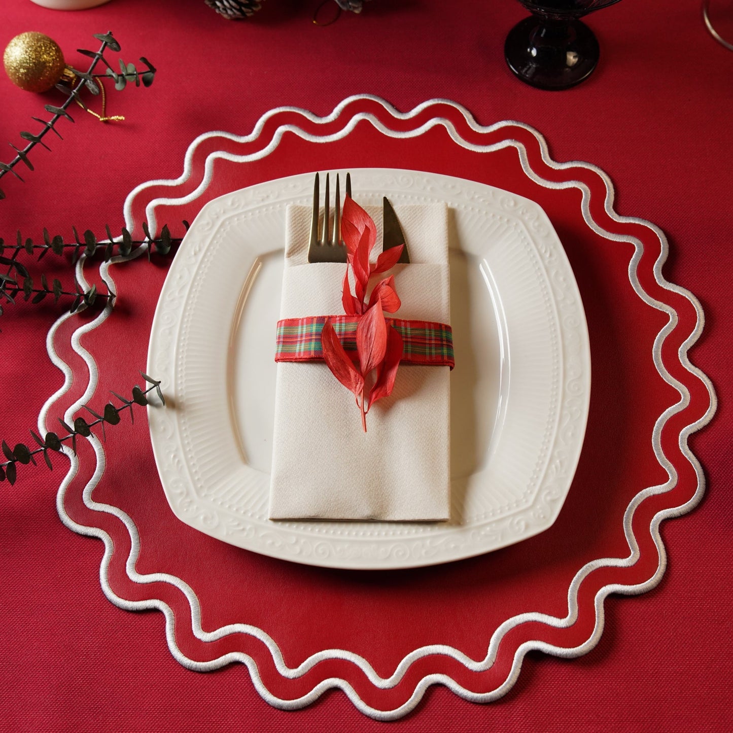Decorative table setting with a white plate, folded napkin, fork, and knife on a red tablecloth.