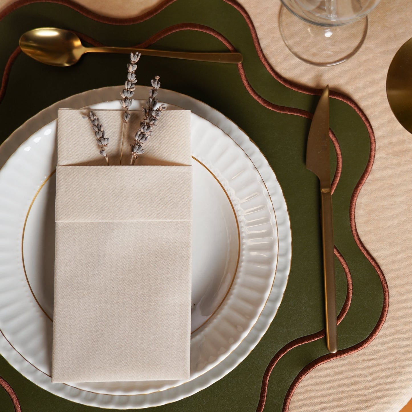 Elegant table setting with gold cutlery, white plates, and a decorative napkin on a green tablecloth.