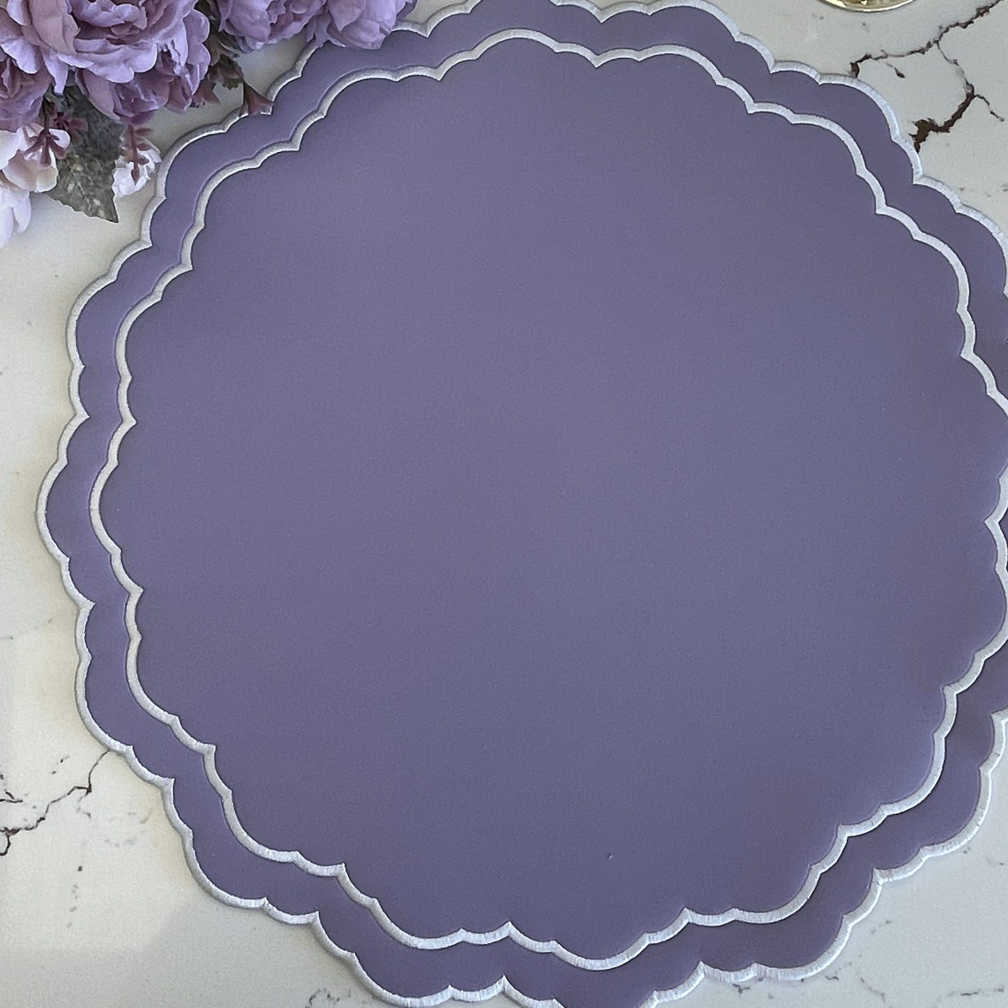 Purple scalloped placemat on a marble surface with flowers and gold coasters.