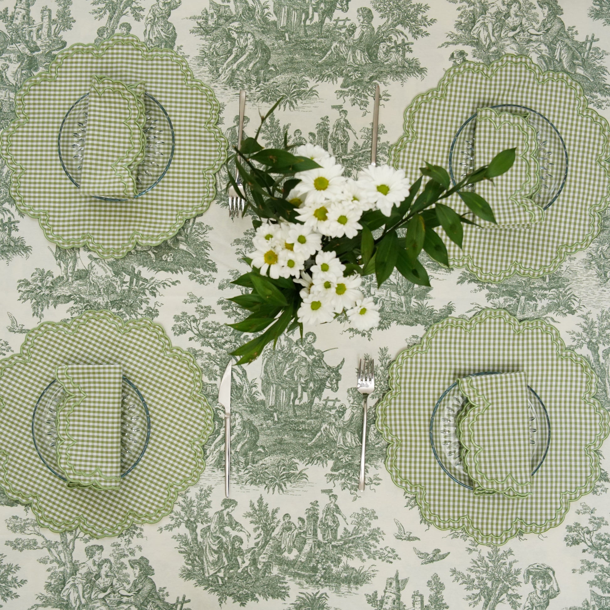 Set of four green checkered placemats on a patterned tablecloth with a floral arrangement.