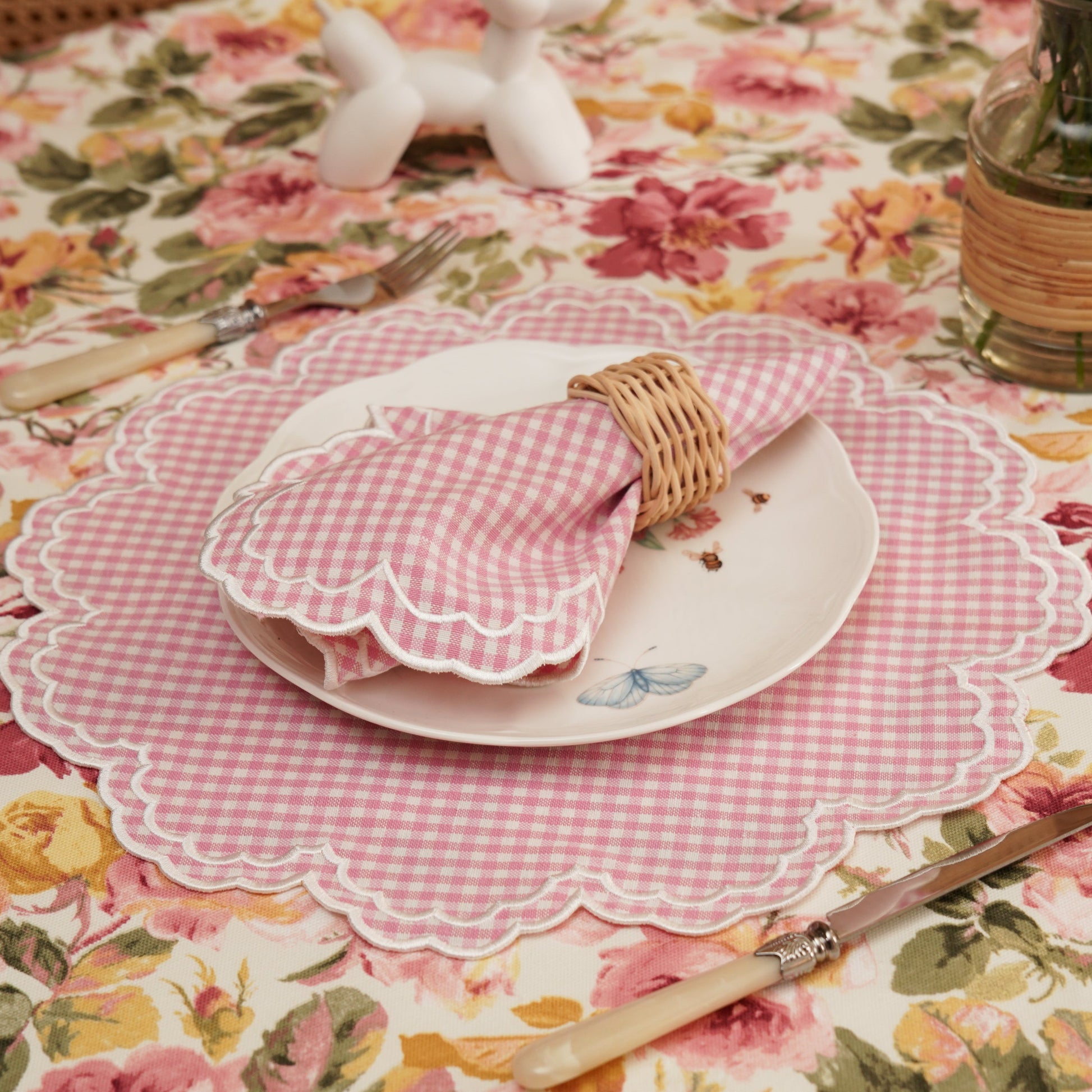 Table setting with floral tablecloth, checkered placemat, and cutlery.