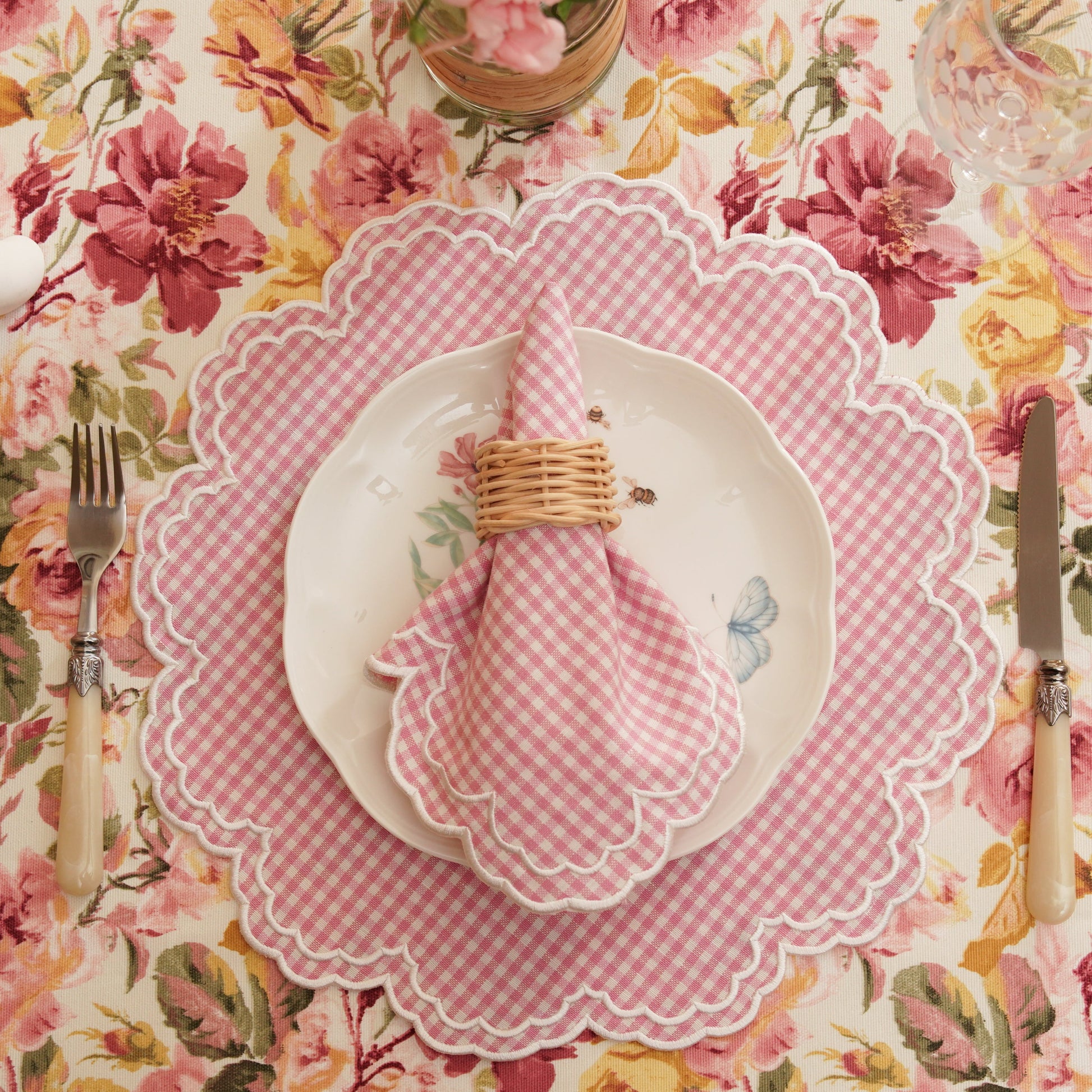 A set of pink and white gingham placemats with floral pattern on a tablecloth, including a napkin tied with a ribbon.