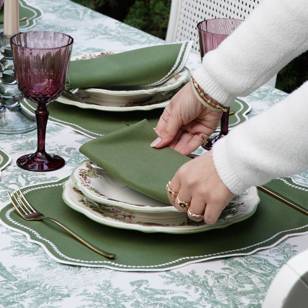 Person setting a table with green plates and purple glasses.