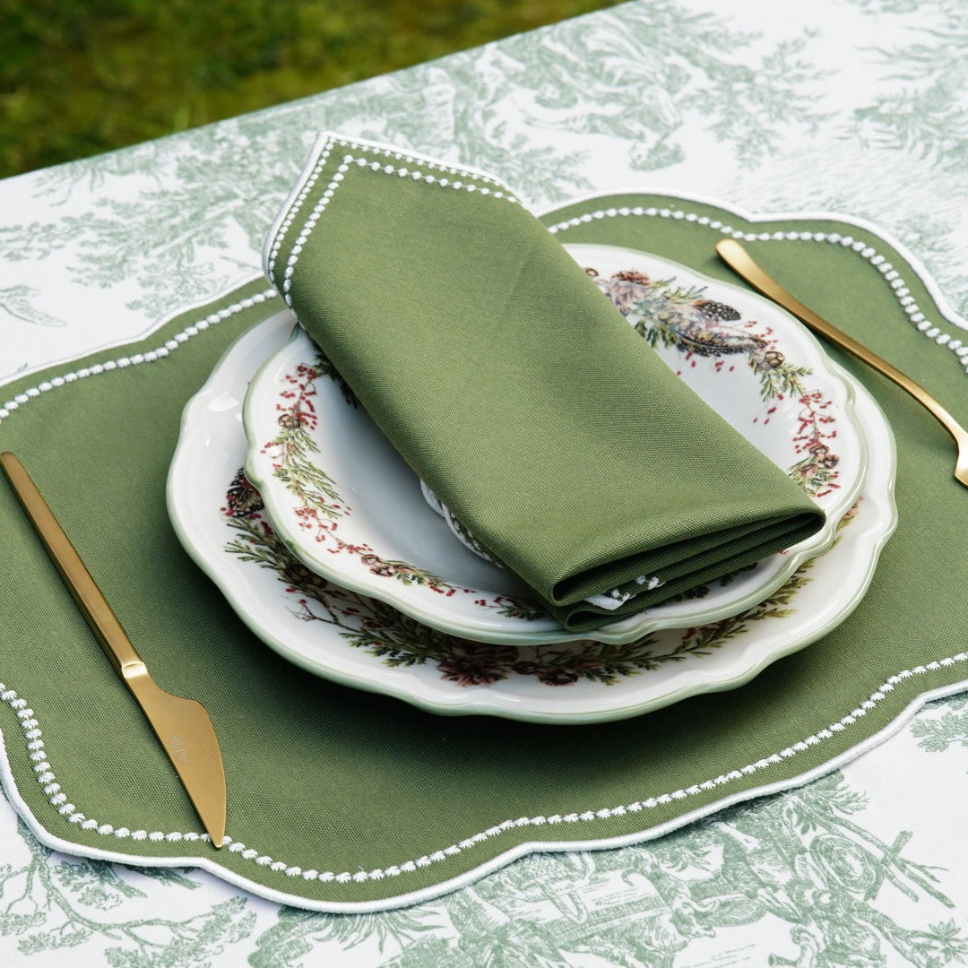 Elegant table setting with green placemats and napkins on a floral tablecloth.