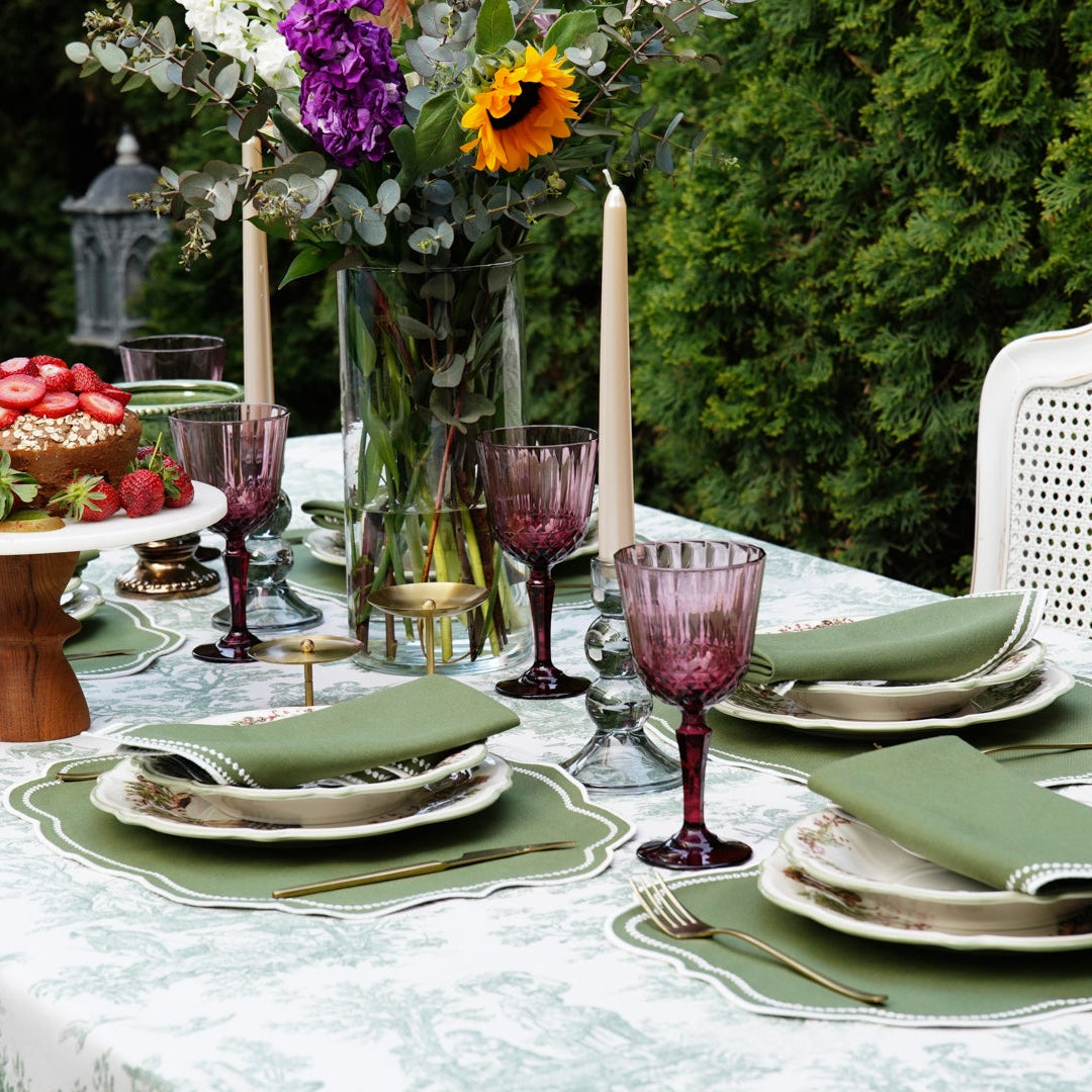 Elegant table setting with green napkins and purple glasses outdoors.