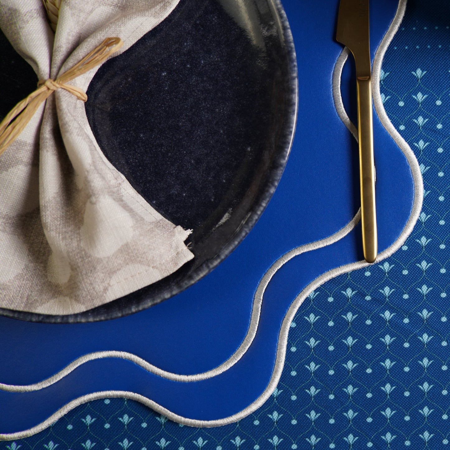 Napkin folded into a decorative shape on a dark plate with a knife on a blue patterned tablecloth.