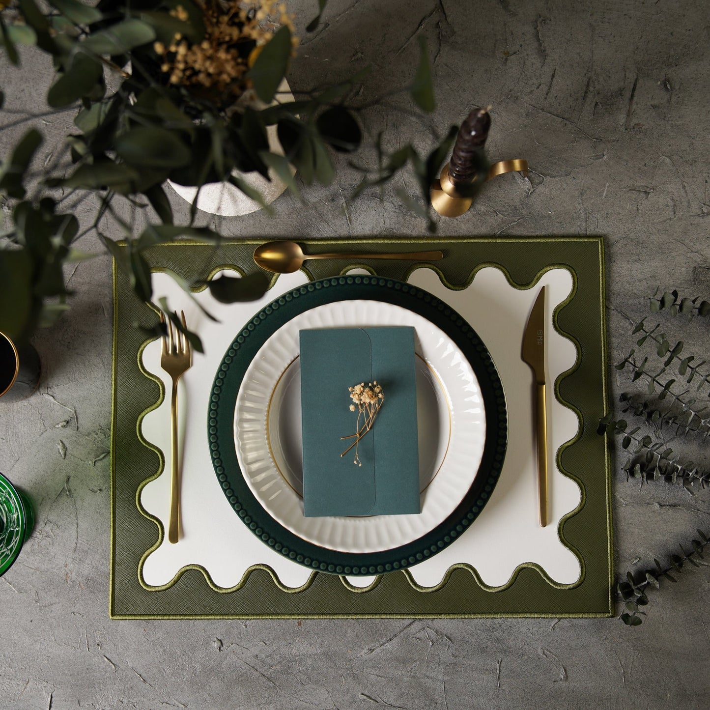 Table setting with green plates, white napkin, and gold cutlery on a textured surface.