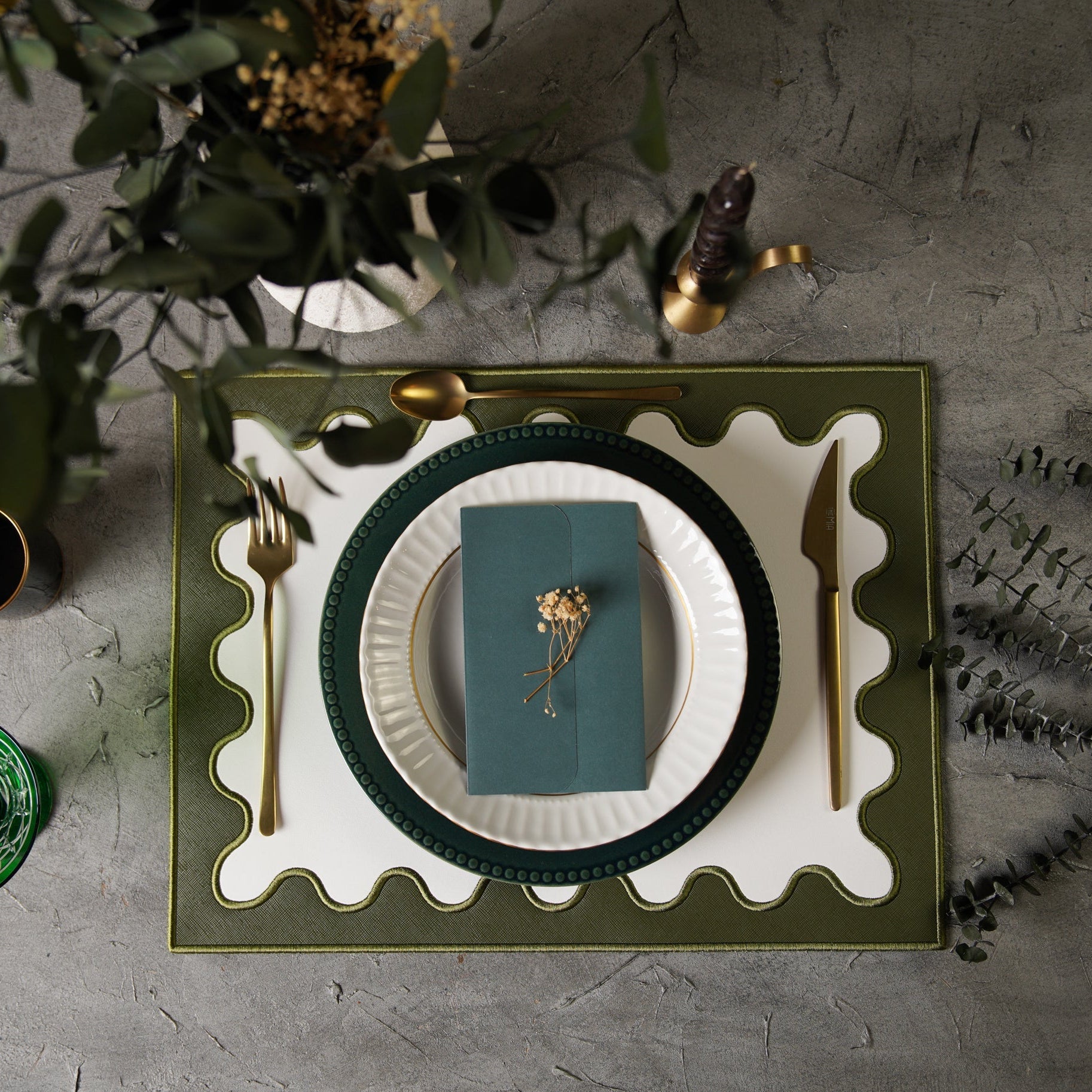 Table setting with green plates, white napkin, and gold cutlery on a textured surface.