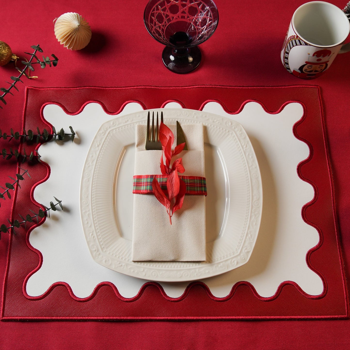 Dining table setting with a red placemat, white plate, and decorative napkin on a red surface.