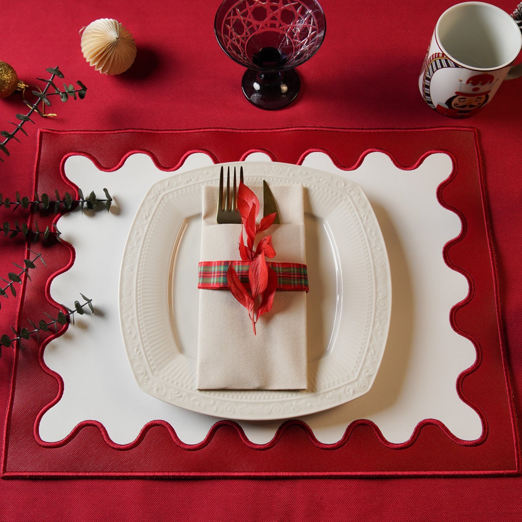 Dining table setting with a red placemat, white plate, and decorative napkin on a red surface.