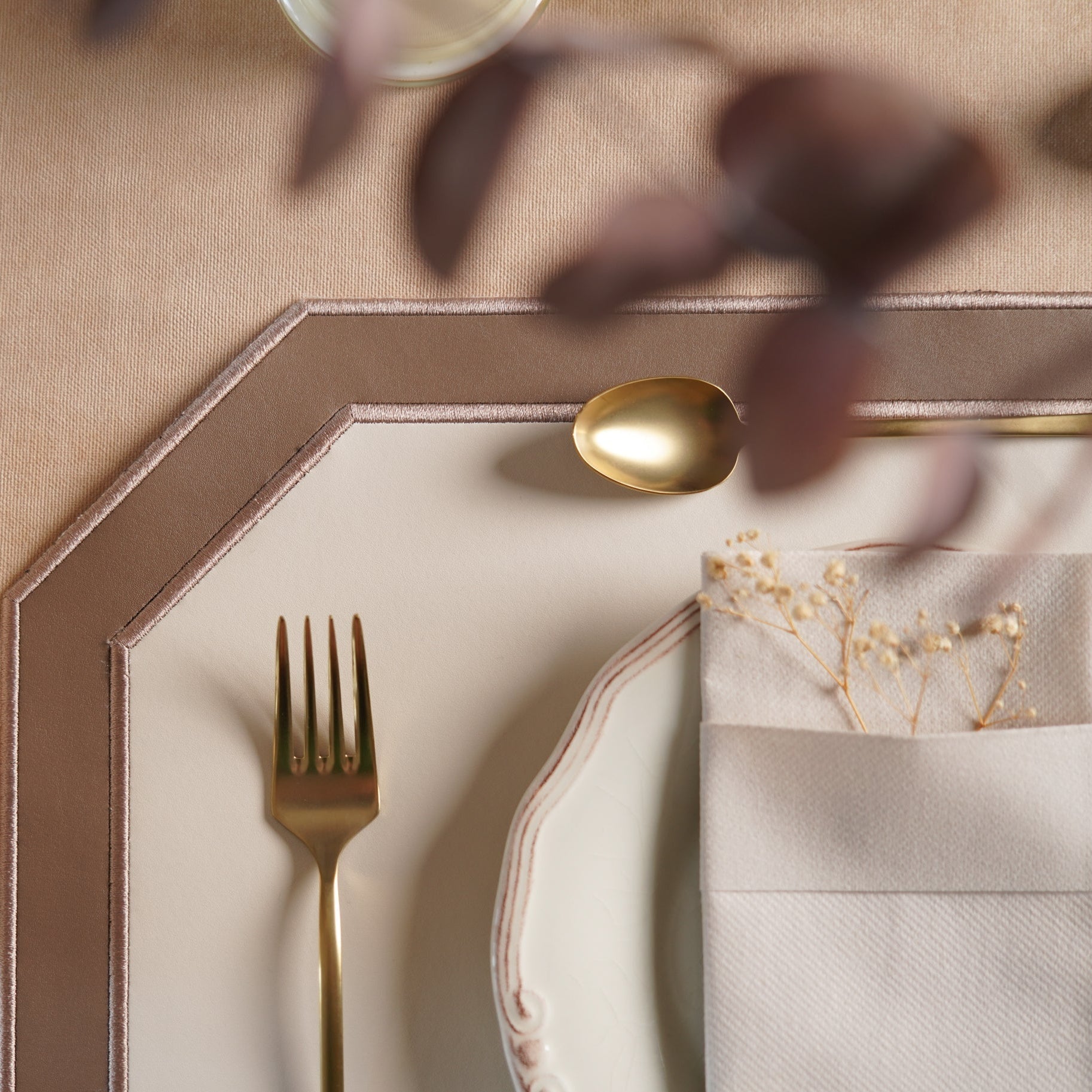 Gold fork and spoon on a beige plate with a decorative napkin and flowers.