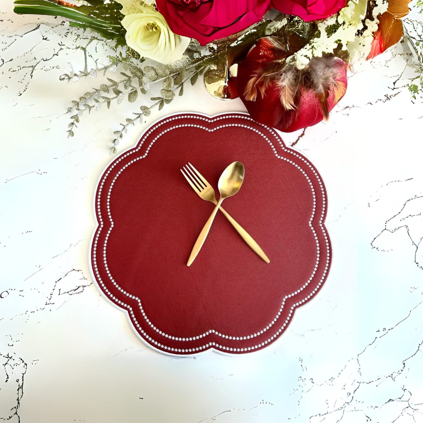 Red placemat with gold fork and spoon on a marble surface with flowers in the background