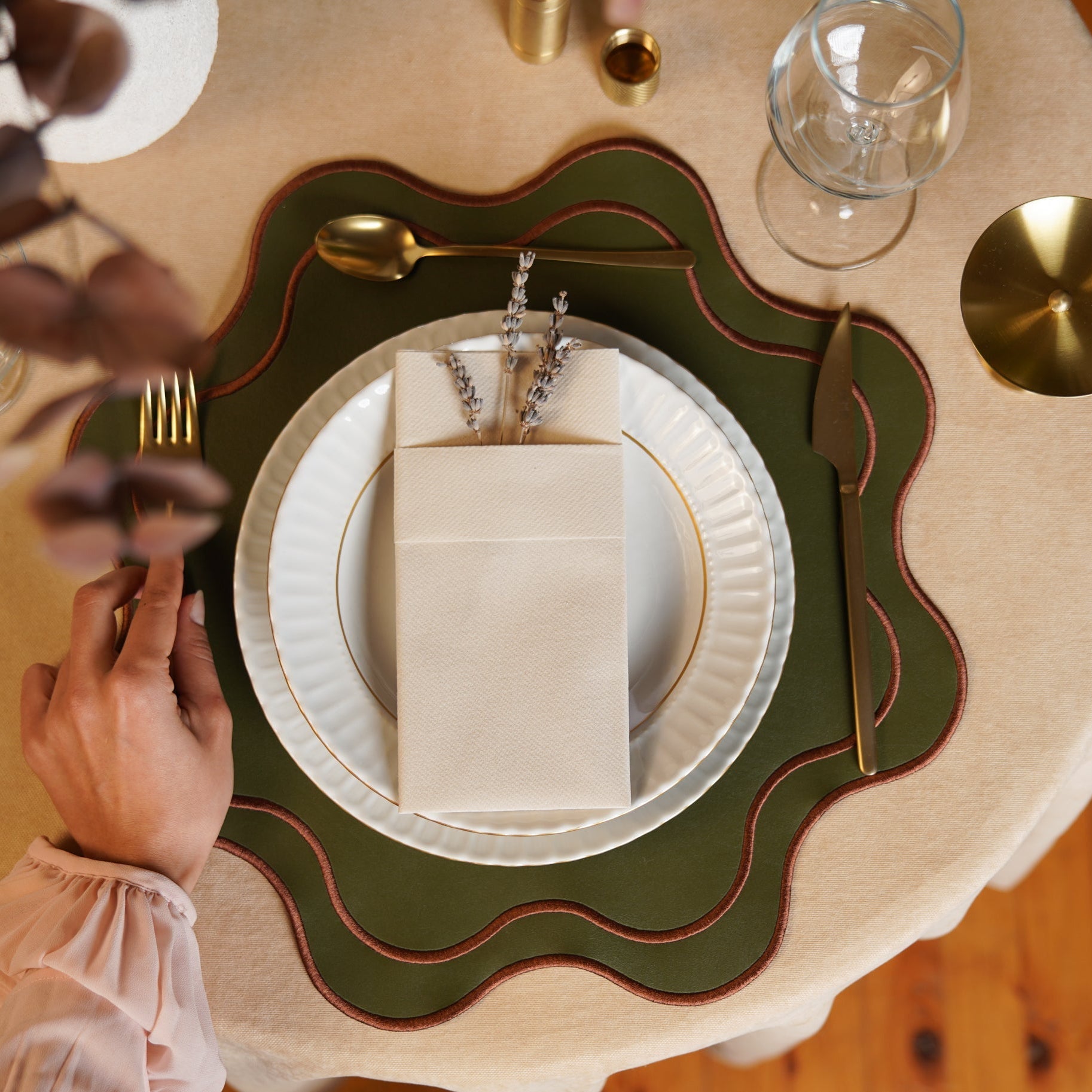 Elegant table setting with green placemat, gold cutlery, and white plates.