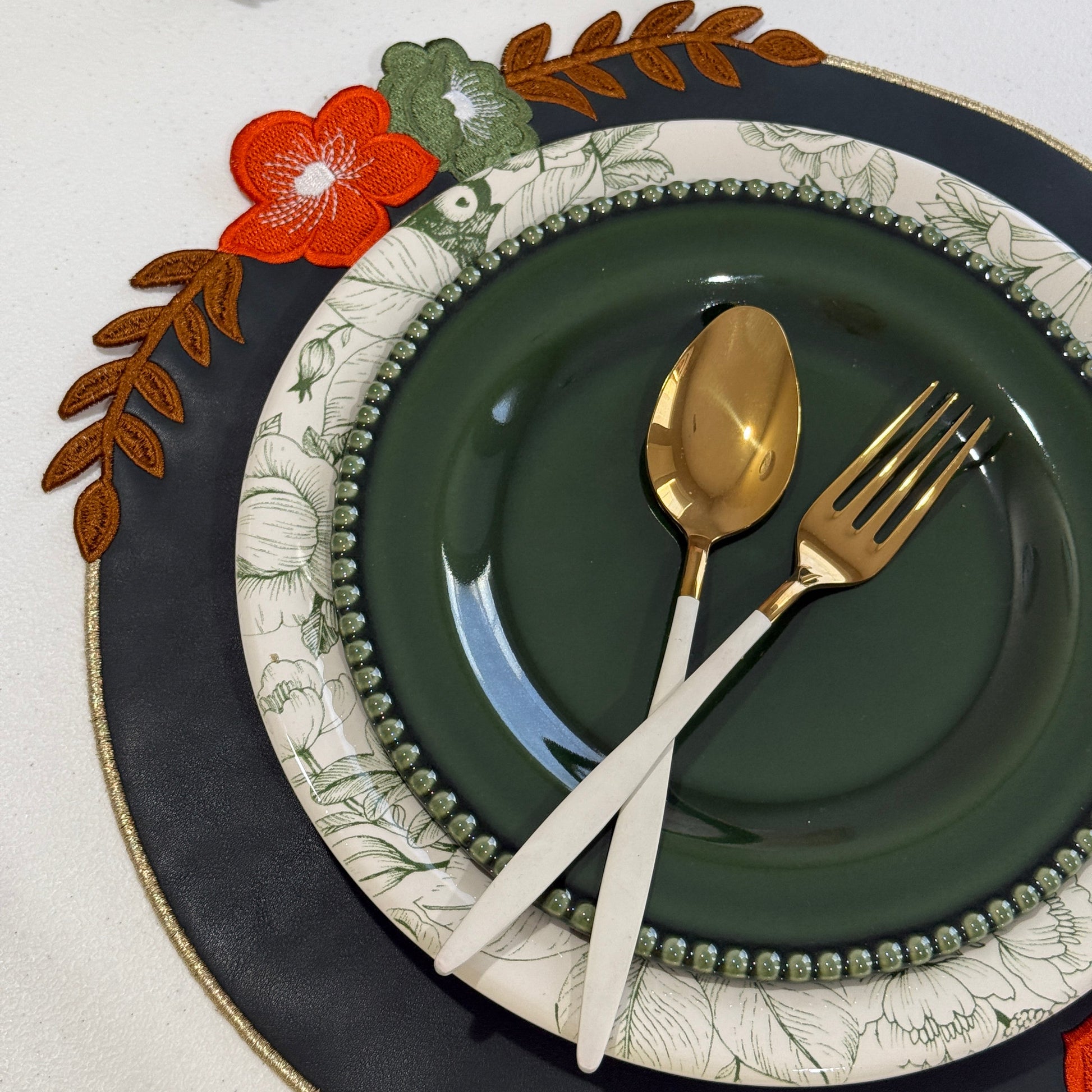 Decorative table setting with green plates, gold spoon, white knife, and floral placemat.