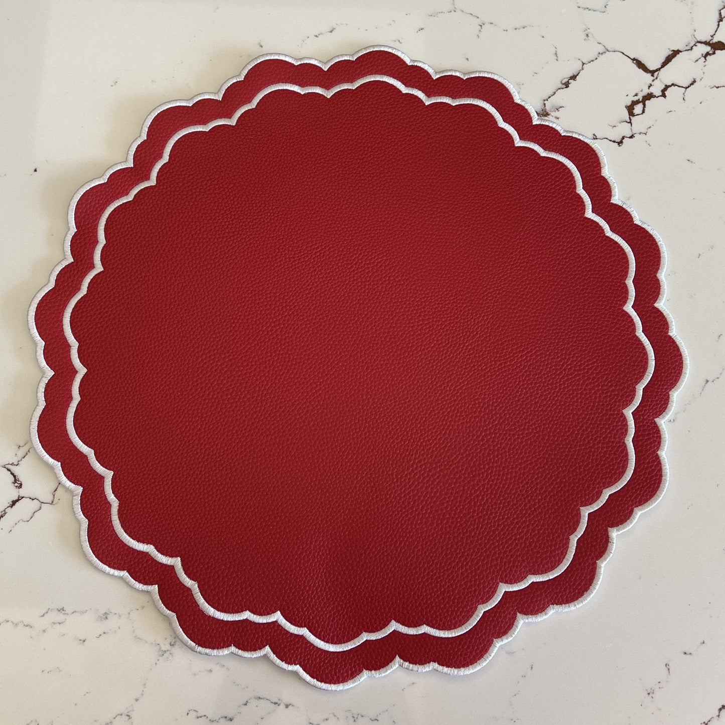 Round red placemat with scalloped edge on a marble surface