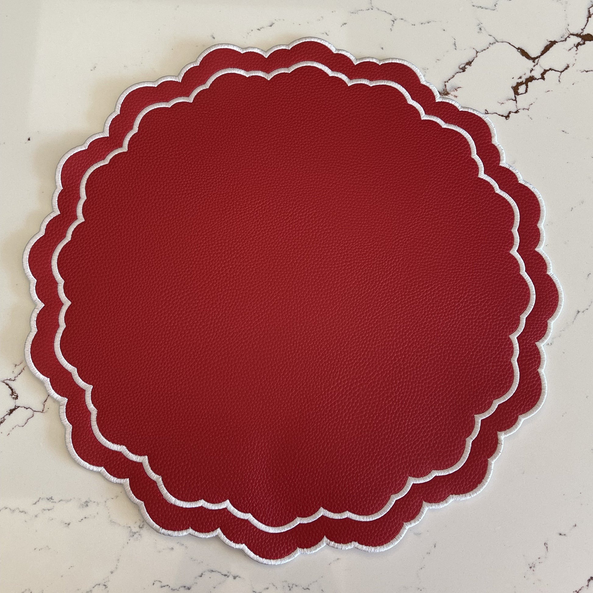 Round red placemat with scalloped edge on a marble surface