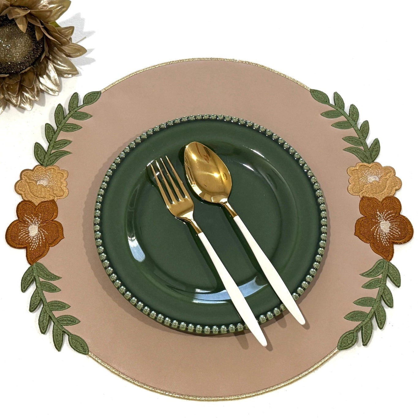 A beige faux leather placemat with embroidered details, presented on a table setting with a green plate and gold cutlery.