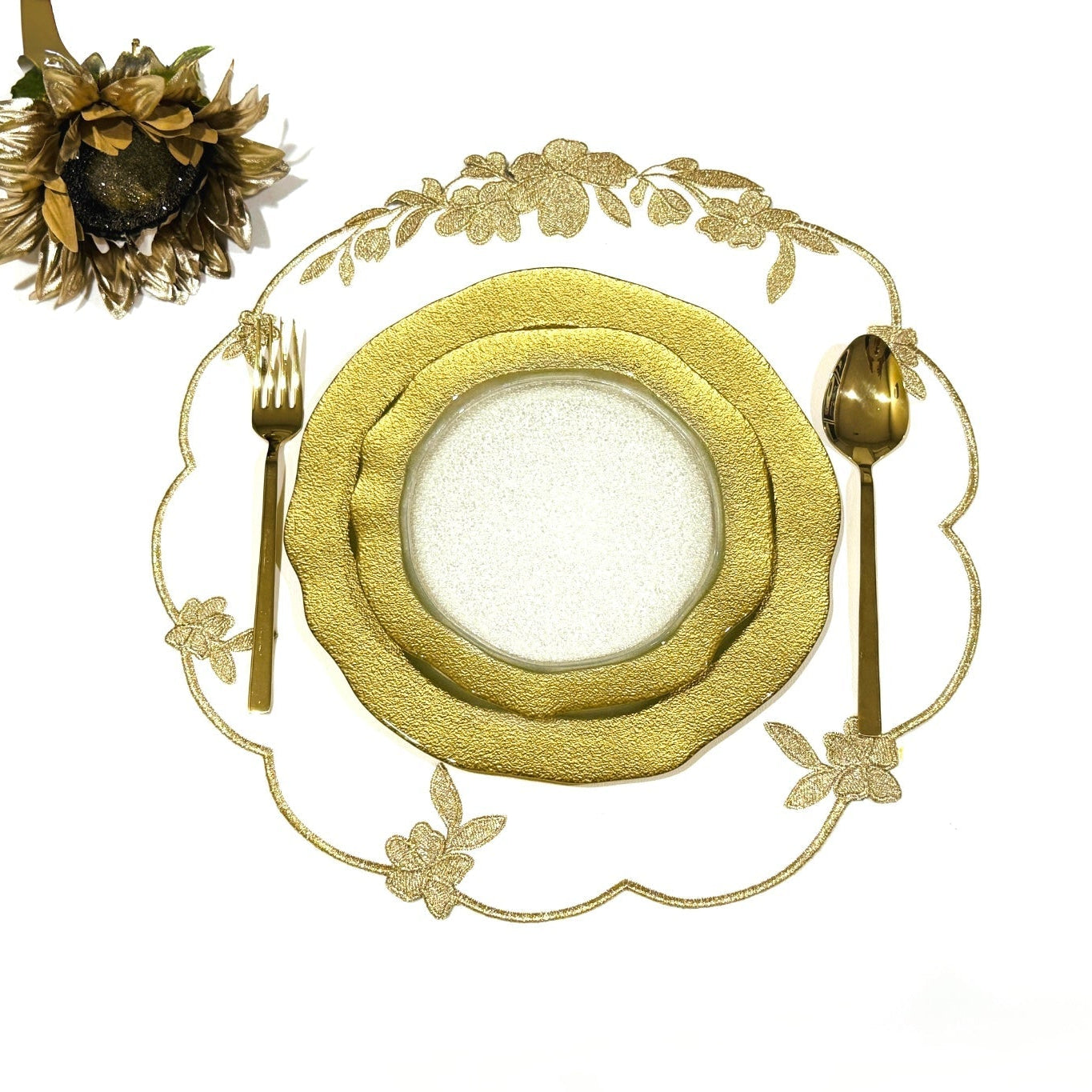 Gold place setting with decorative plates, cutlery, and a floral arrangement on a white background.