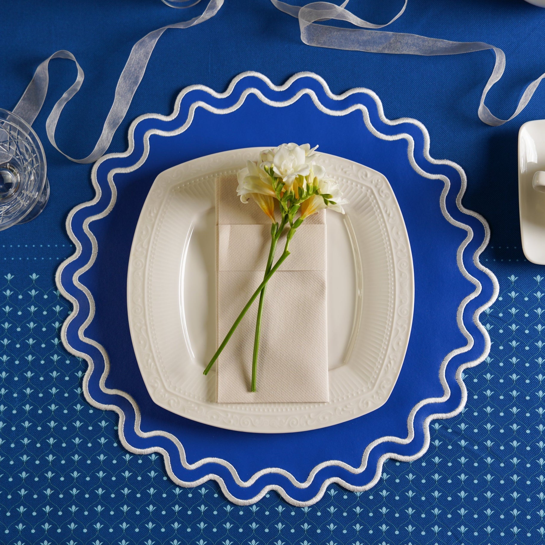 White plate with a flower on a blue tablecloth