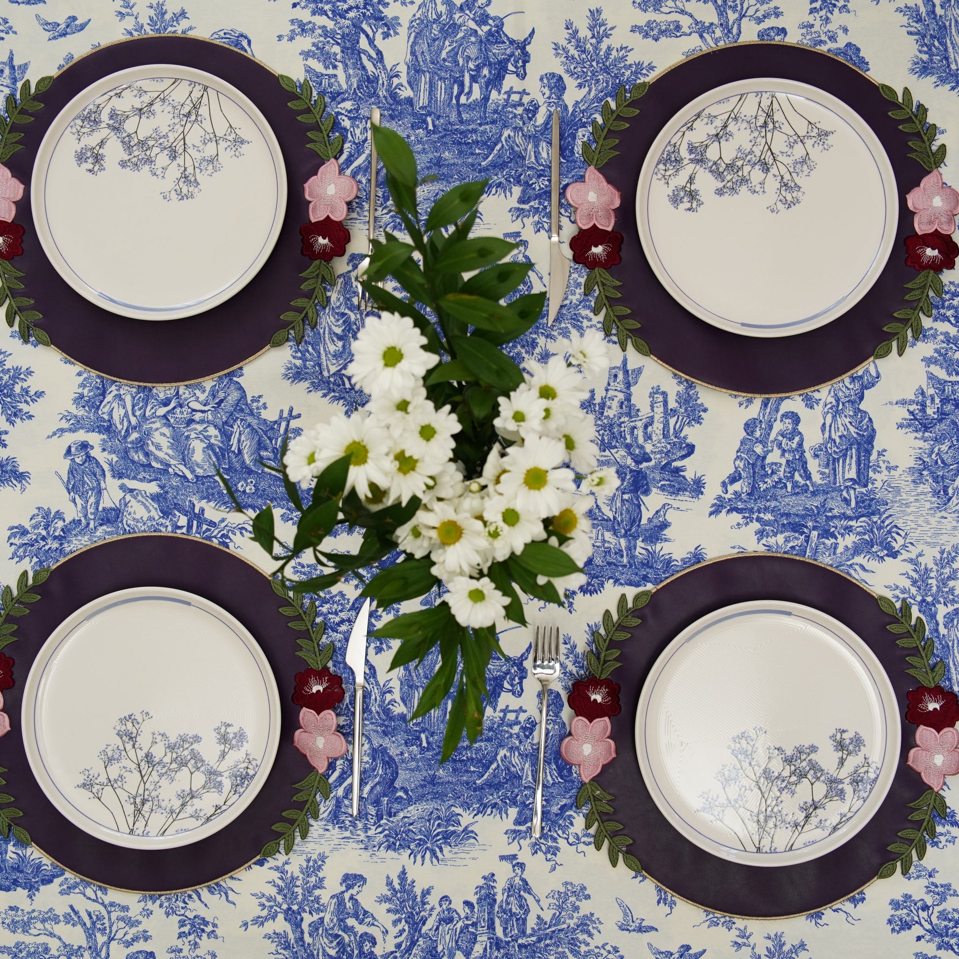 Four place settings with floral decorations on a blue and white patterned tablecloth.