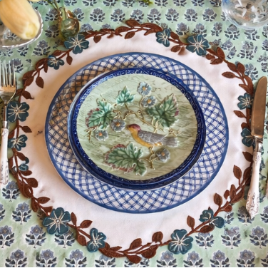 Decorative table setting with a patterned plate featuring birds, on a matching tablecloth.